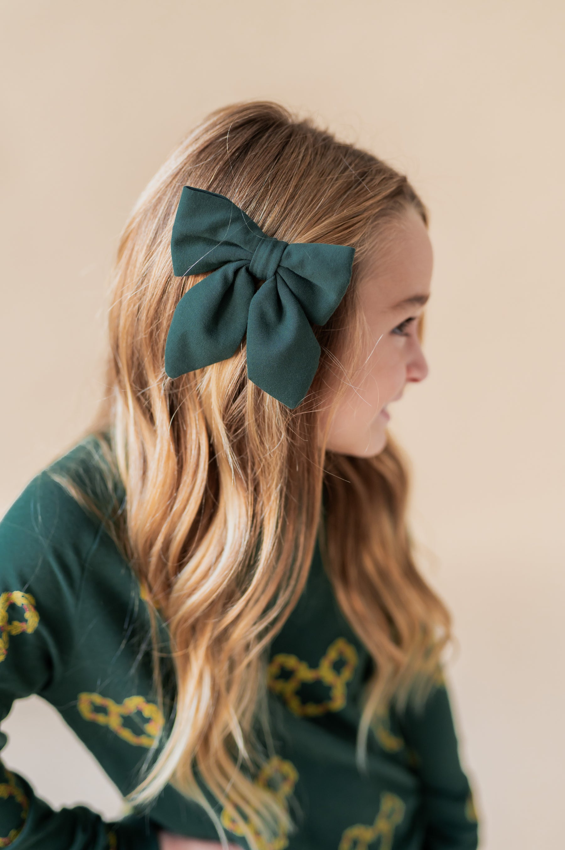 Girl wearing Medium Alligator Clip Bow in Cypress color in her hair on a beige background