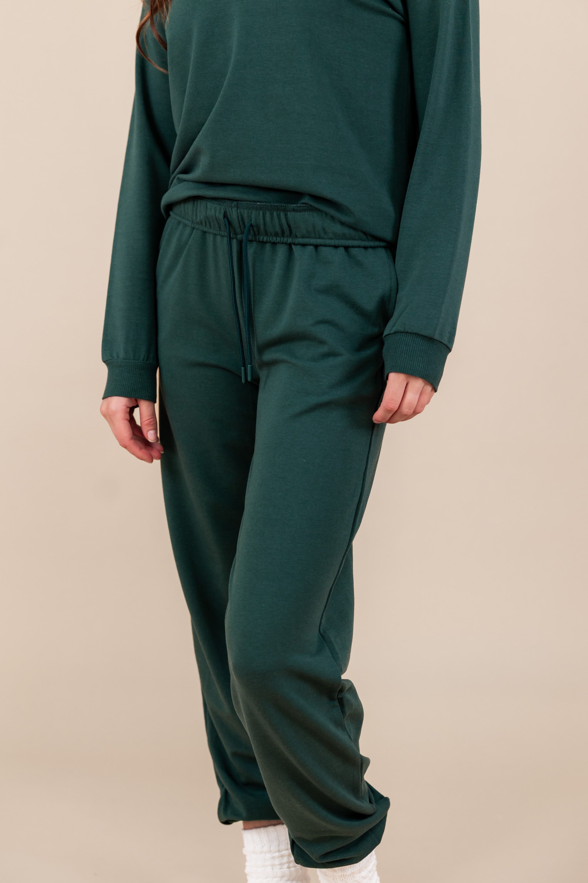 Modal wearing Women's Jogger Pant in Cypress color under similar color sweatshirt on a beige background