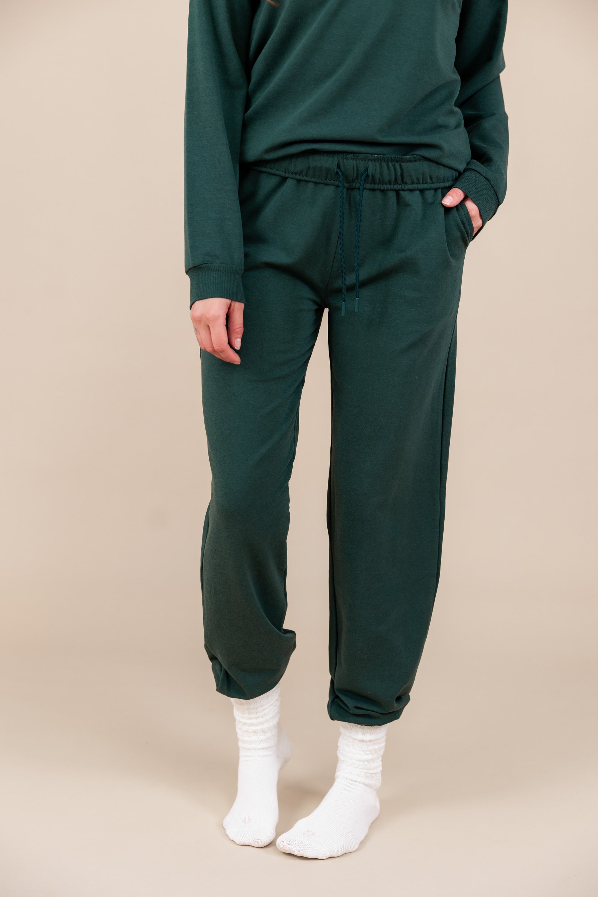 Modal wearing Women's Jogger Pant in Cypress color with pockets under similar color sweatshirt on a beige background