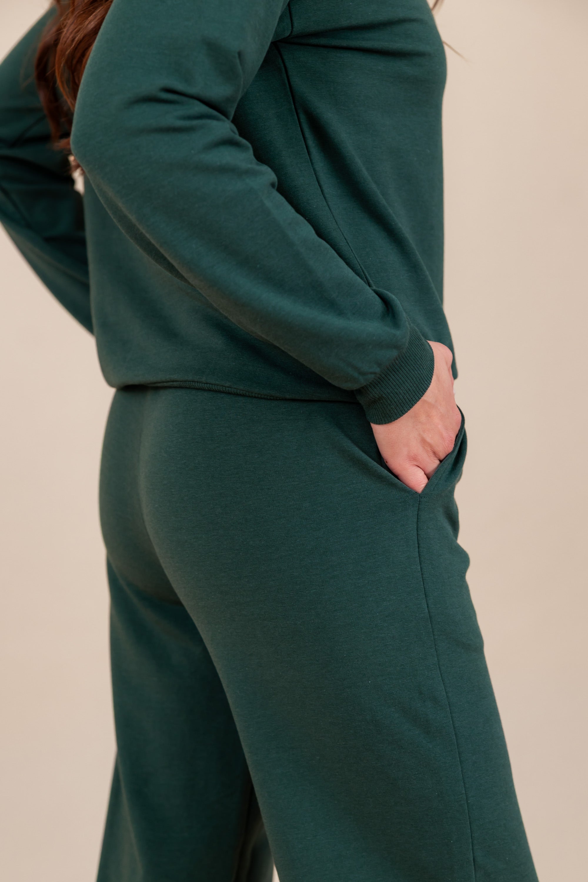 Side view of Modal wearing Women's Jogger Pant in Cypress color with pockets under similar color sweatshirt on a beige background