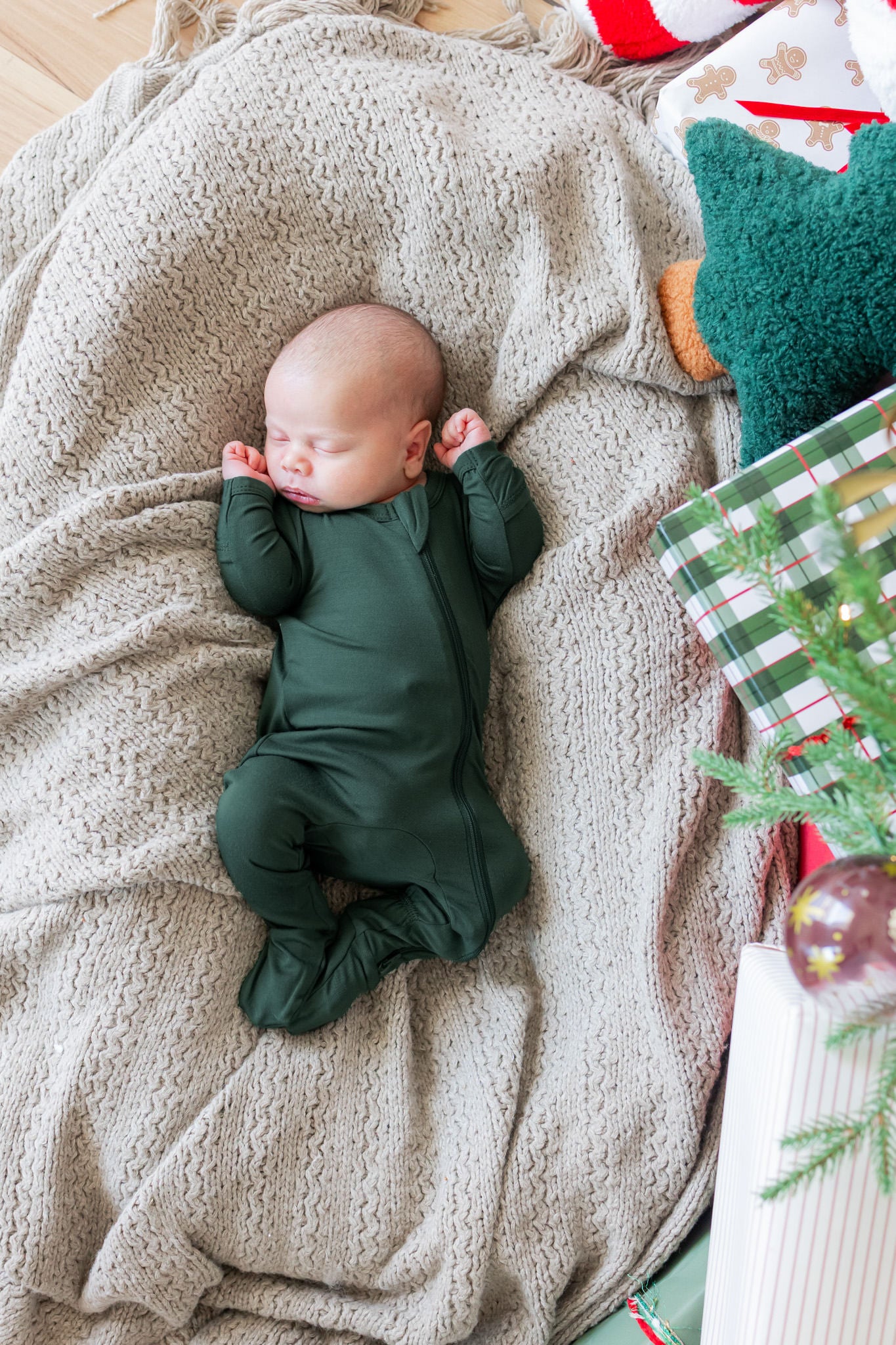 Baby wearing zippered footie in cypress color sleeping on a beige blanket