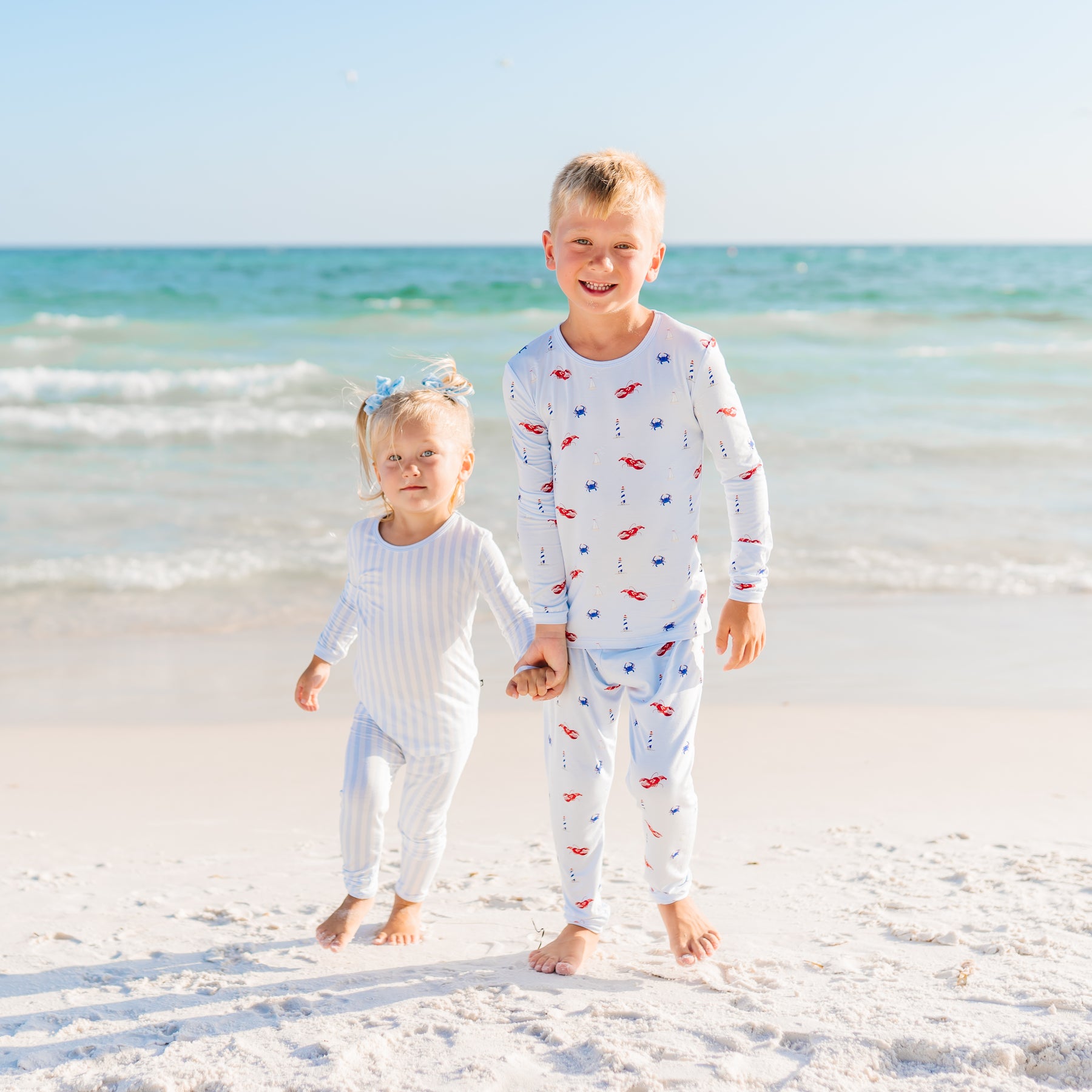 Two children in pajamas standing on a beach with ocean in the background