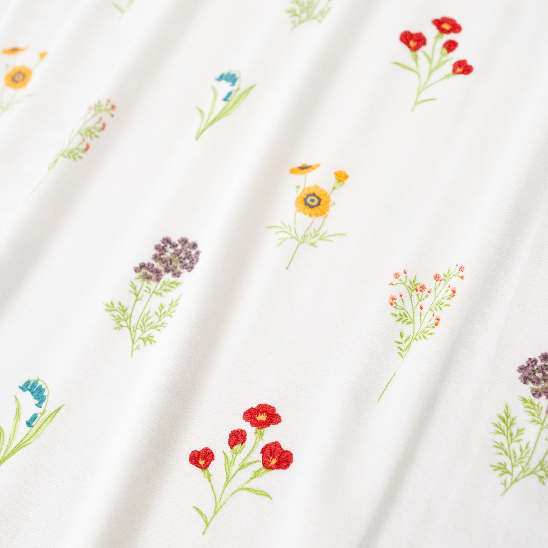 Close up of bamboo fabric: An all-over, repeating print featuring sprigs of light purple Queen Anne’s Lace, dusty blue bluebells, orange globe mallow, yellow coreopsis, and red clarkia over a white background.