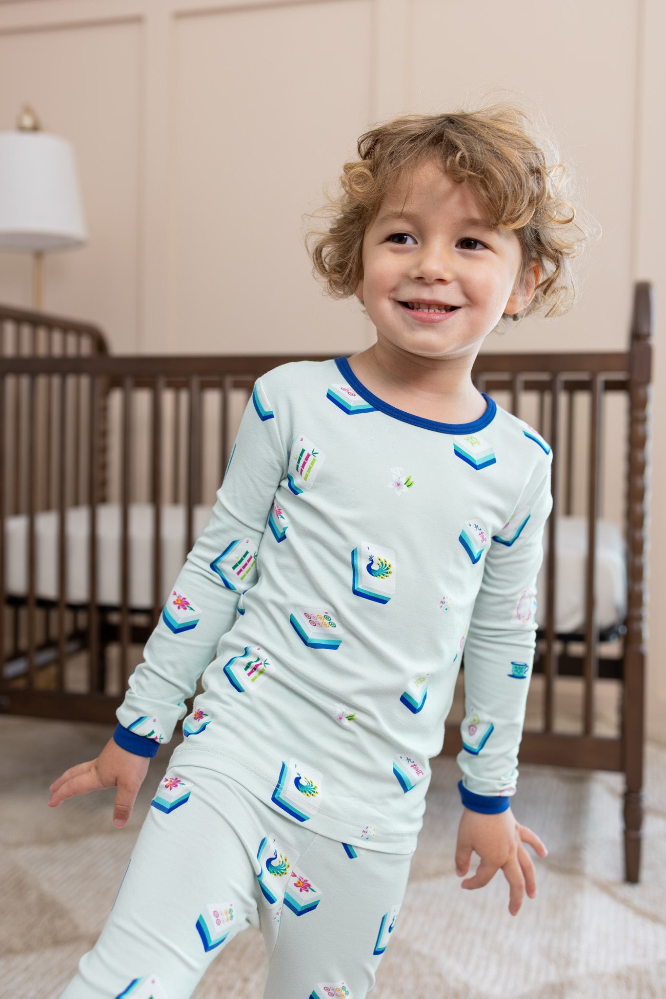 Boy wearing Long Sleeve Pajamas in Dew Mahjong print in front of a crib