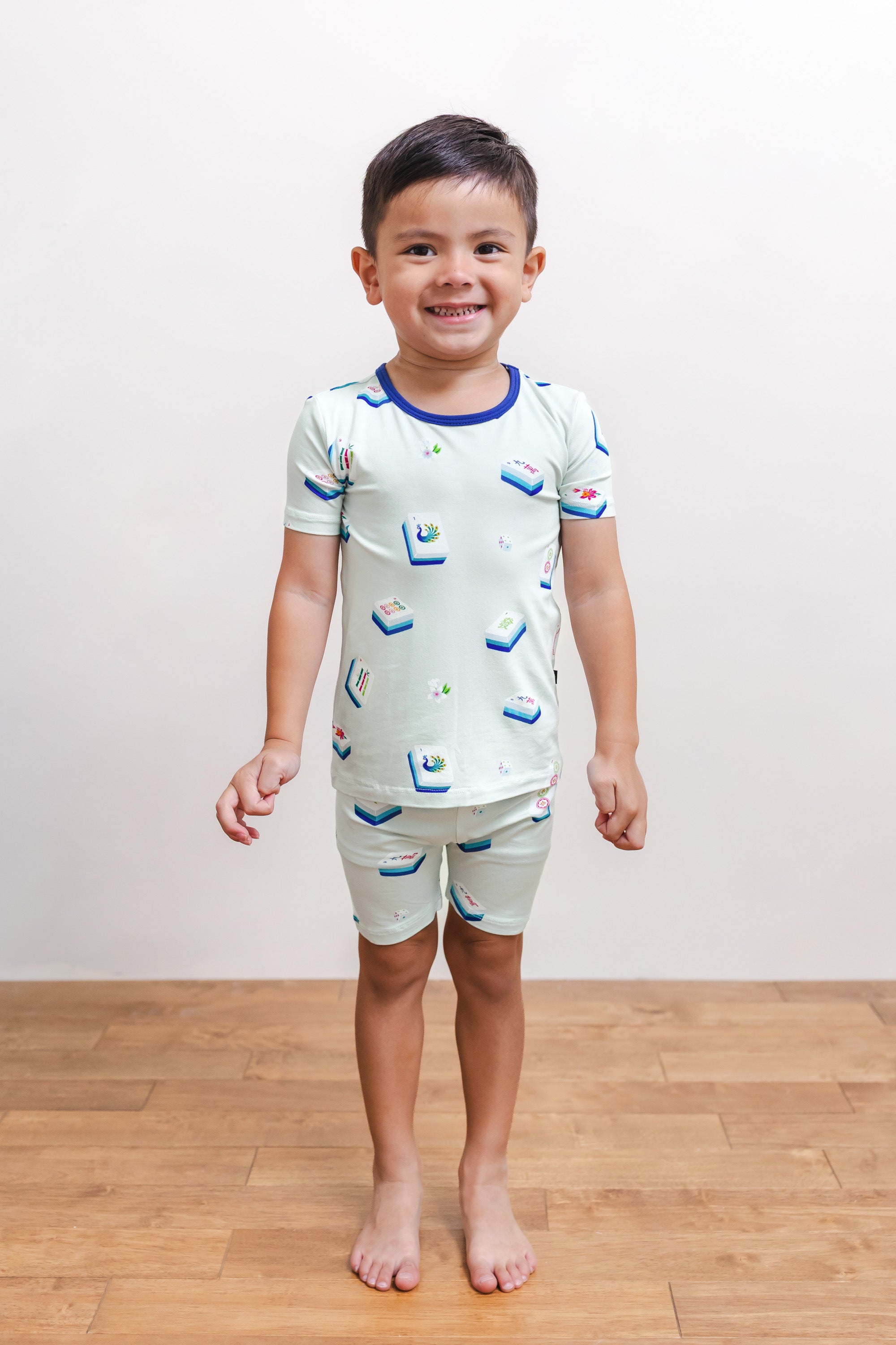 Boy smiling in Short Sleeve Pajamas in Dew Mahjong print against a beige background