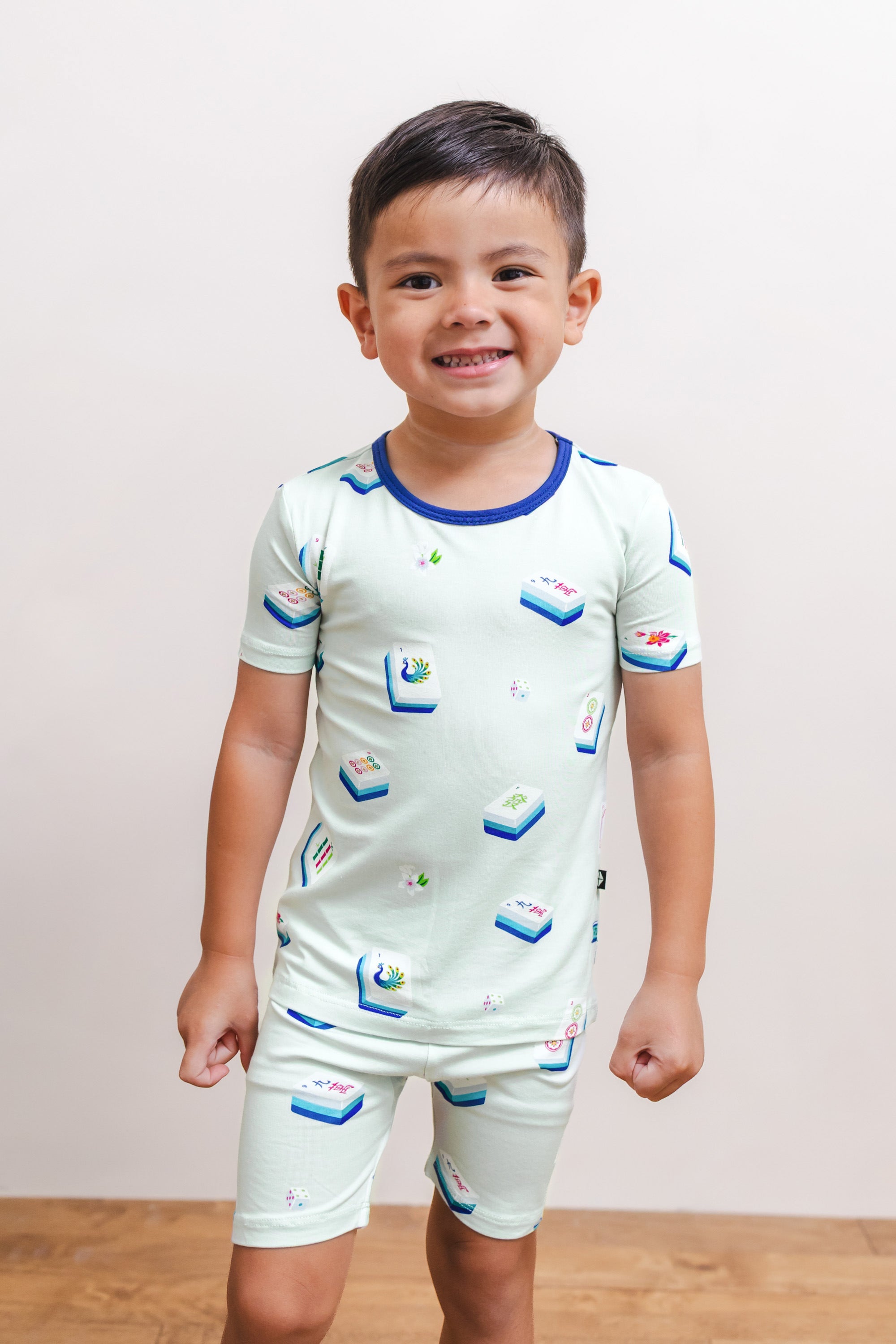 Boy posing in Short Sleeve Pajamas in Dew Mahjong print against a beige background