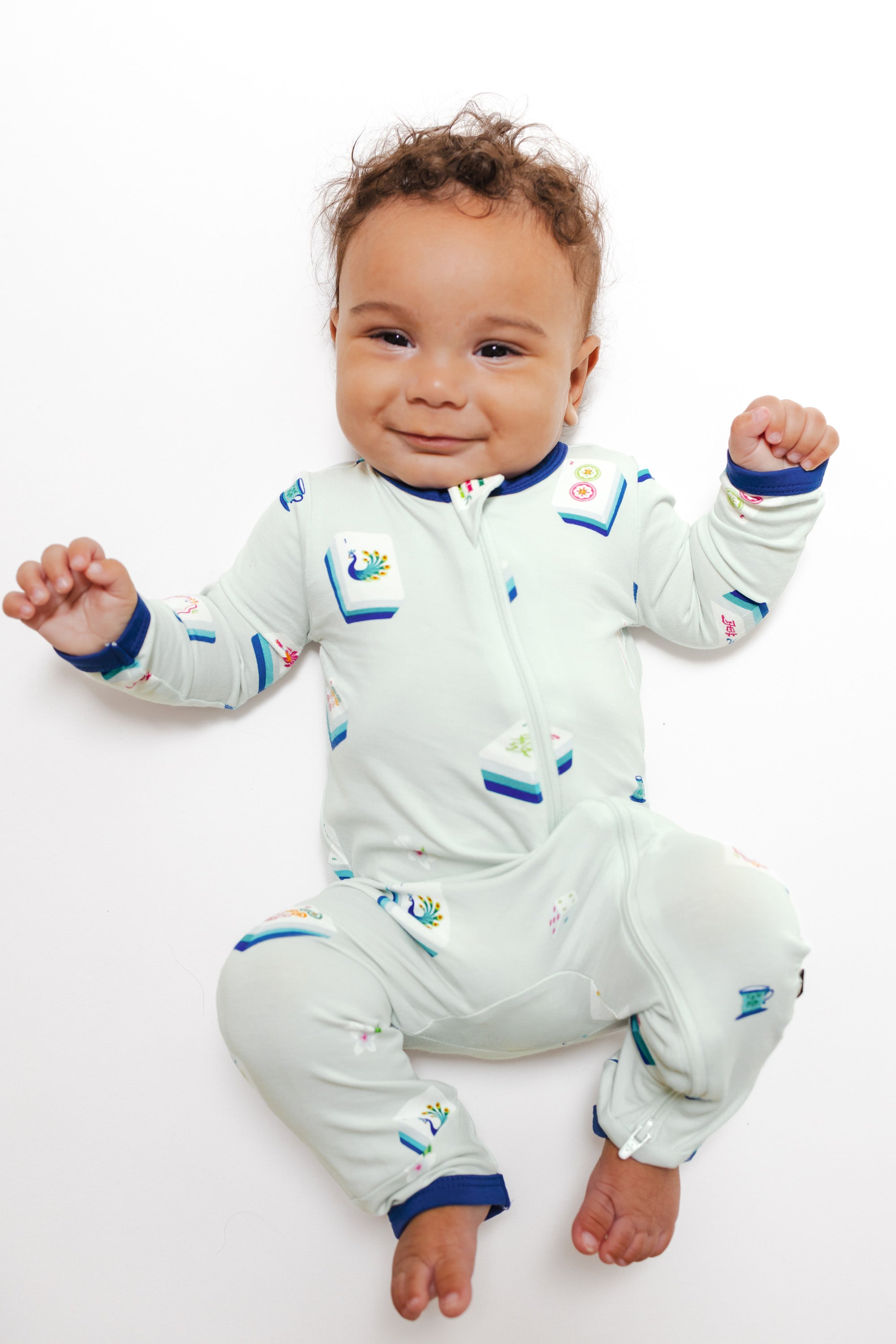Baby smiling in Zippered Romper in Dew Mahjong print lying on a white background