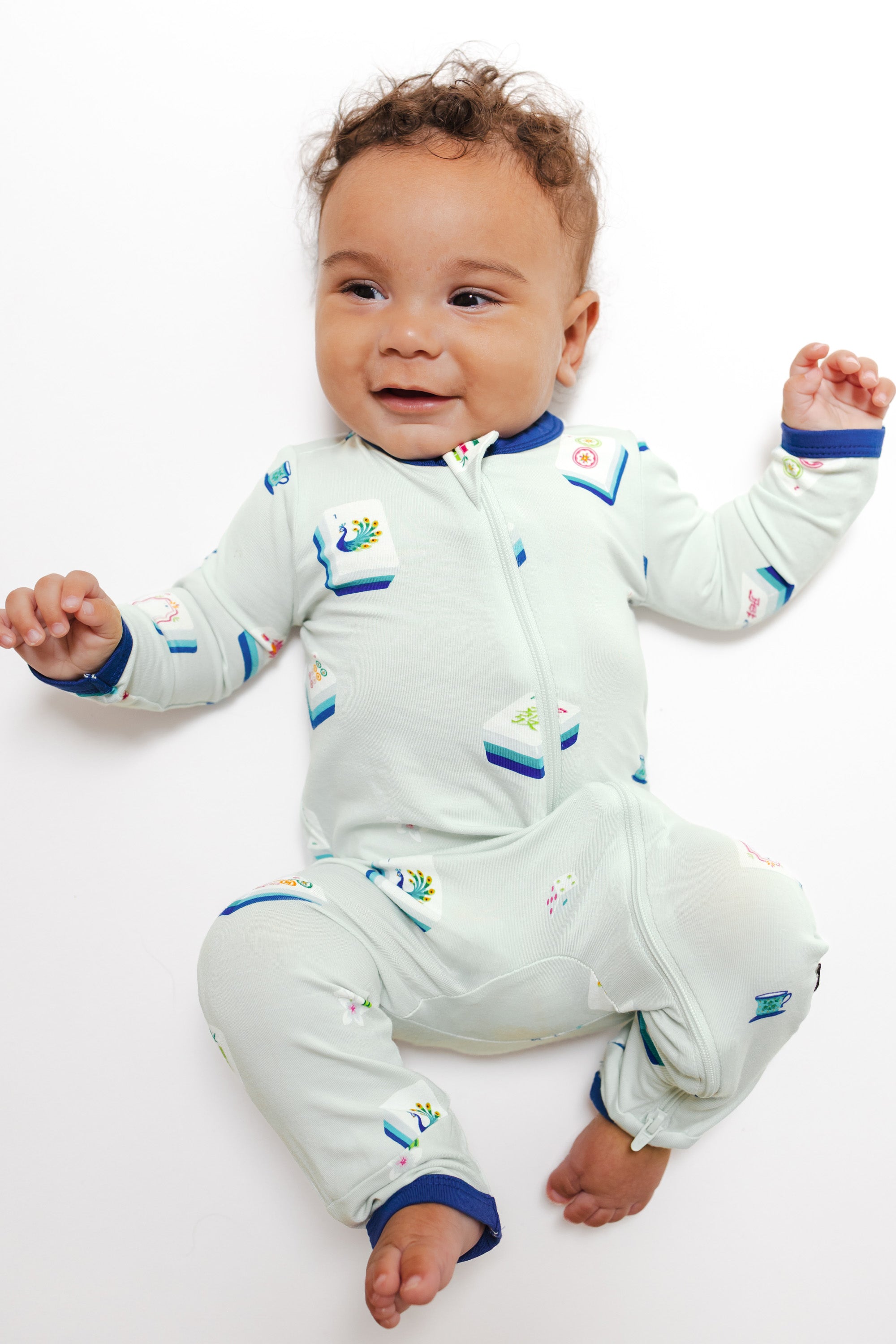 Baby wearing Zippered Romper in Dew Mahjong print lying on a white background