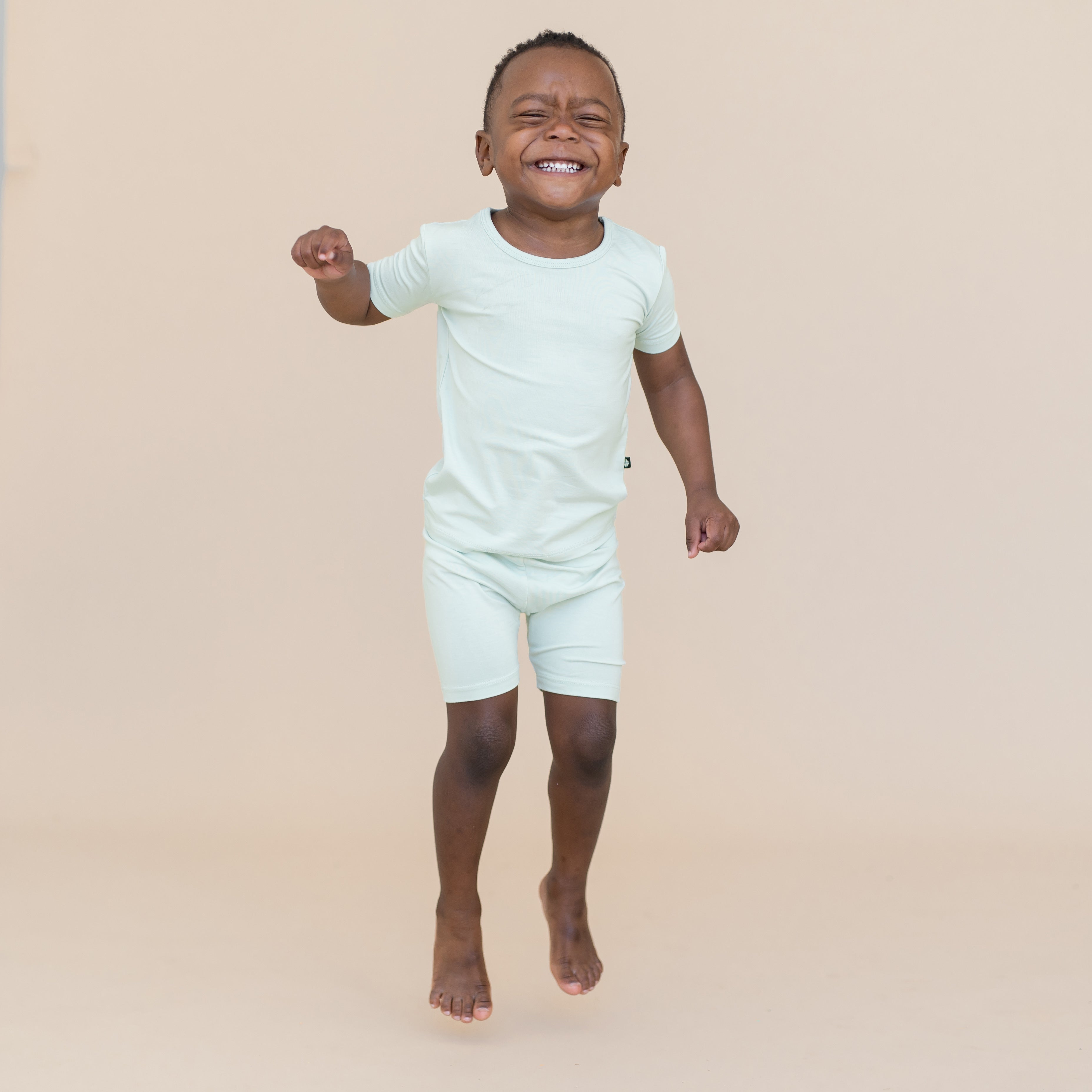 Young boy jumping and wearing a light blue-green short sleeve pajama set