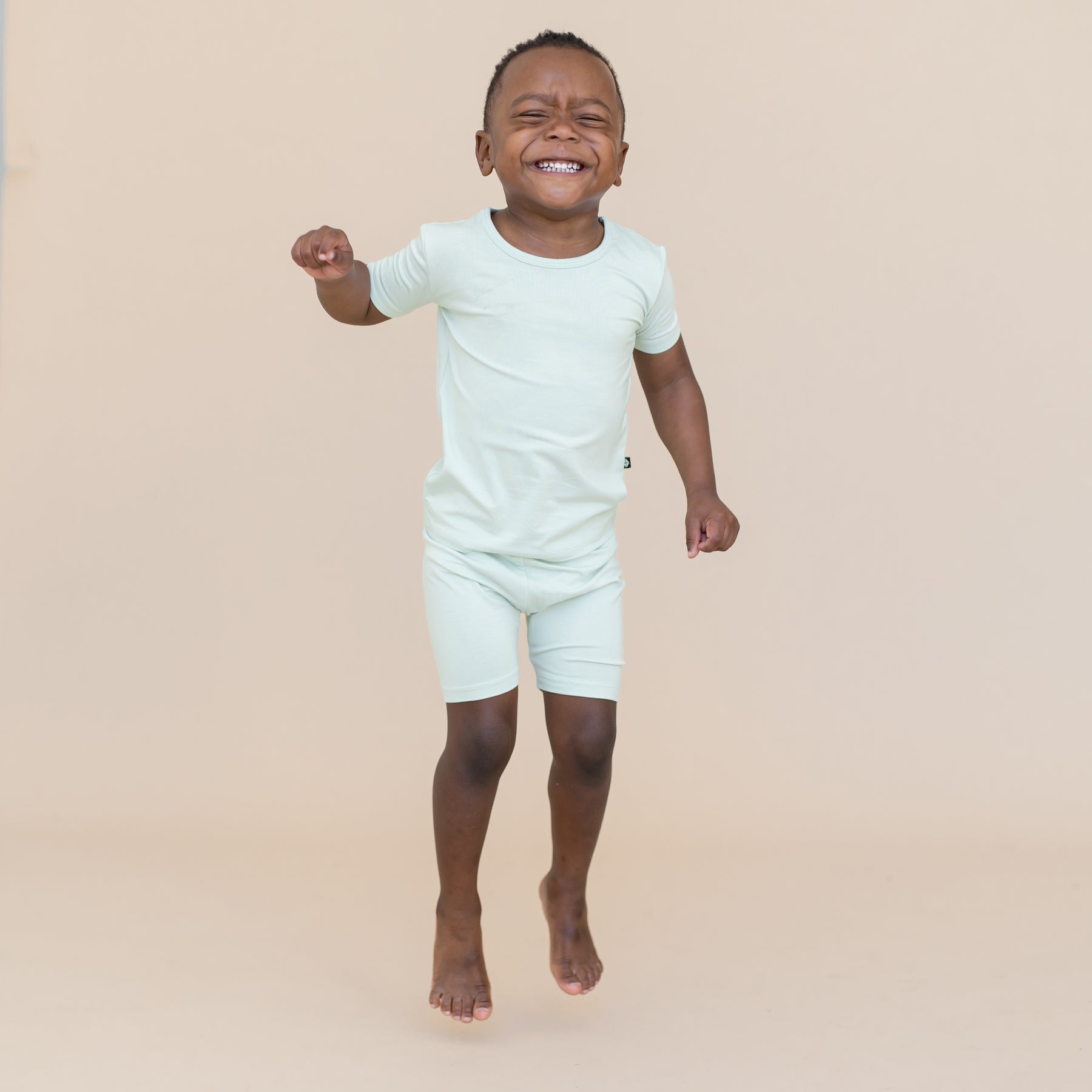 Young boy jumping and wearing a light blue-green short sleeve pajama set