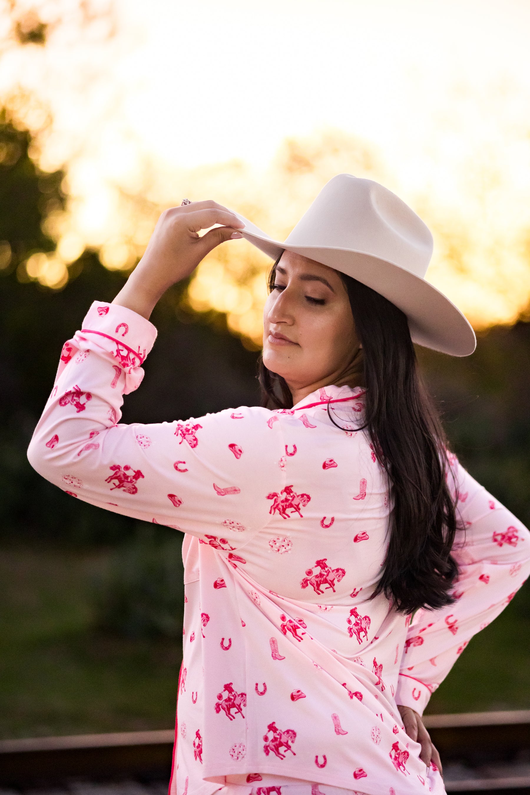 Woman wearing a pink cowgirl pajamas and white cowboy hat with a blurred natural background