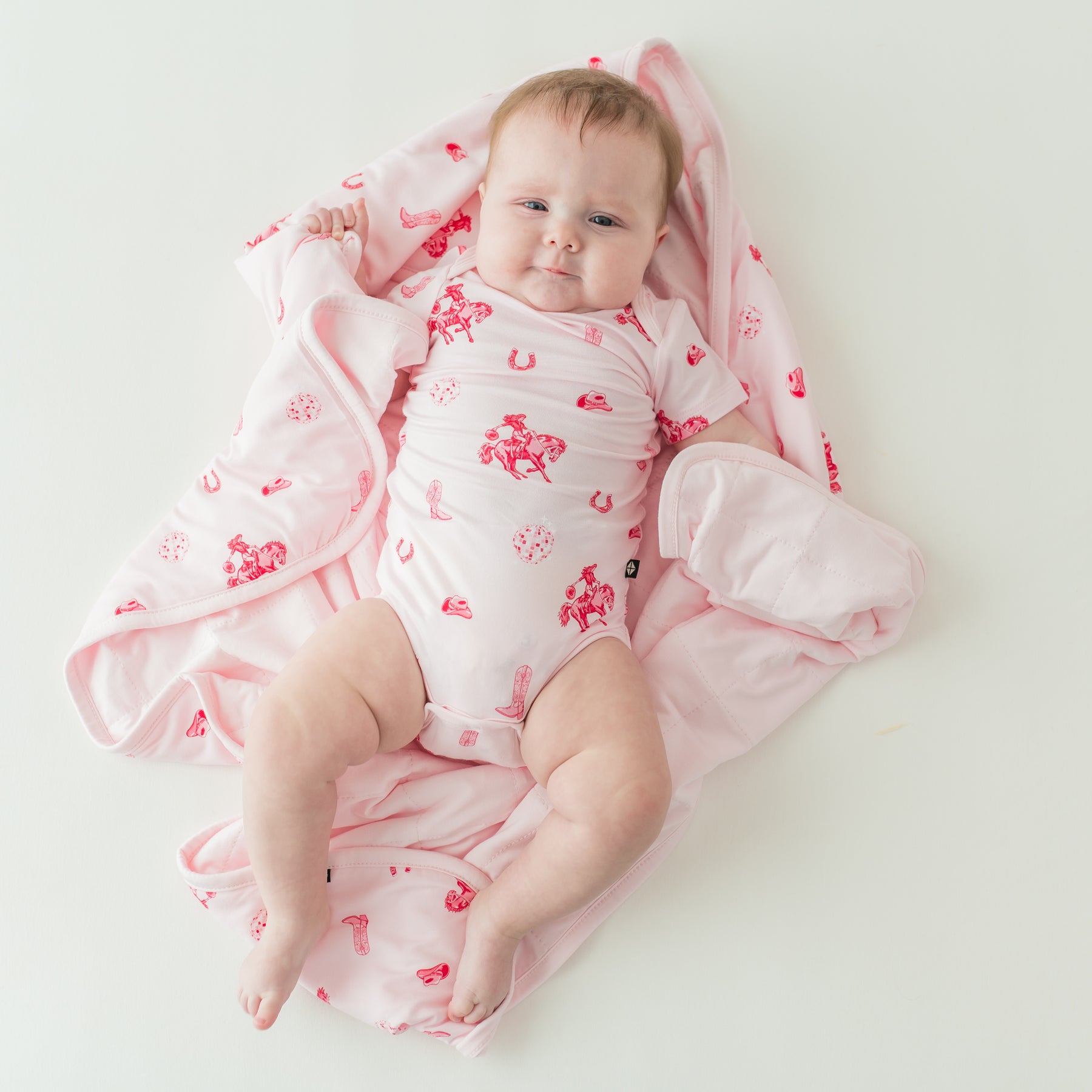 Infant girl wearing the Bodysuit in Disco Cowgirl laying on a matching baby blanket