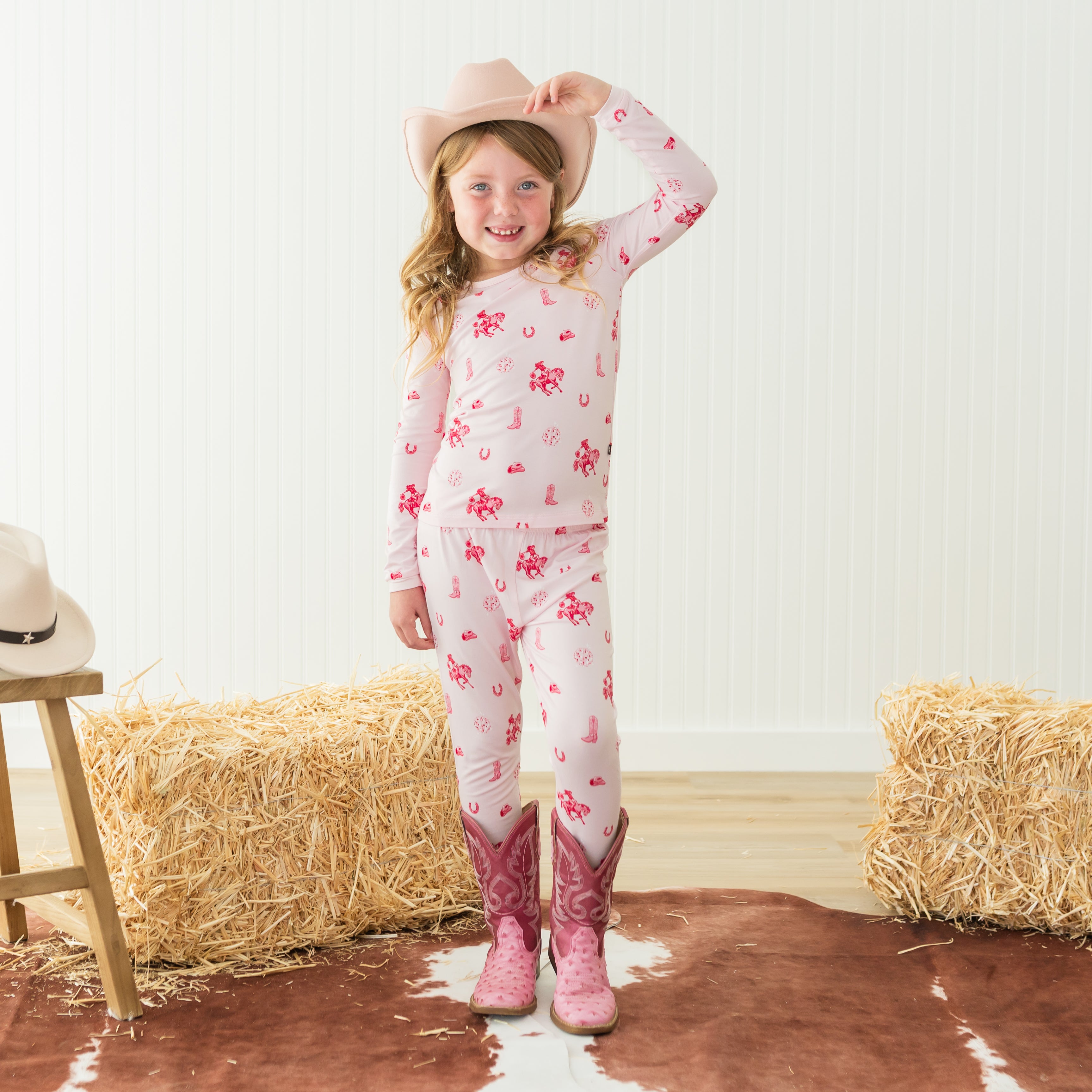 Young girl wearing the Long Sleeve Pajamas in Disco Cowgirl with a pink cowboy hat and pink cowboy boots