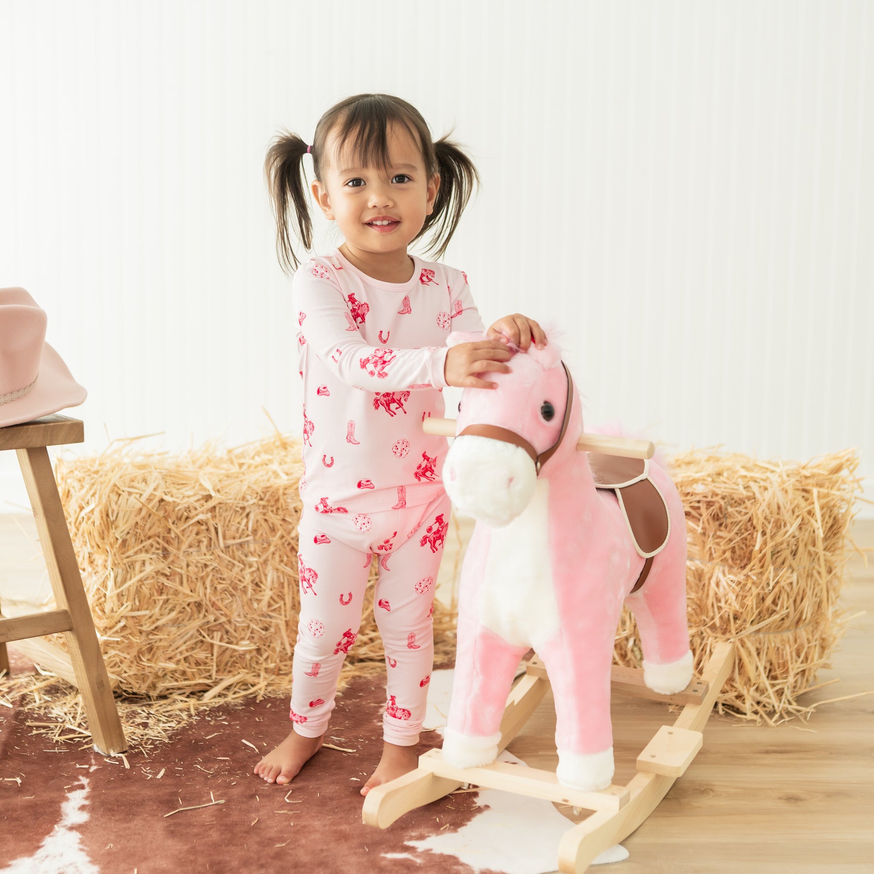Toddler wearing the Long Sleeve Pajamas in Disco Cowgirl standing beside a toy rocking horse