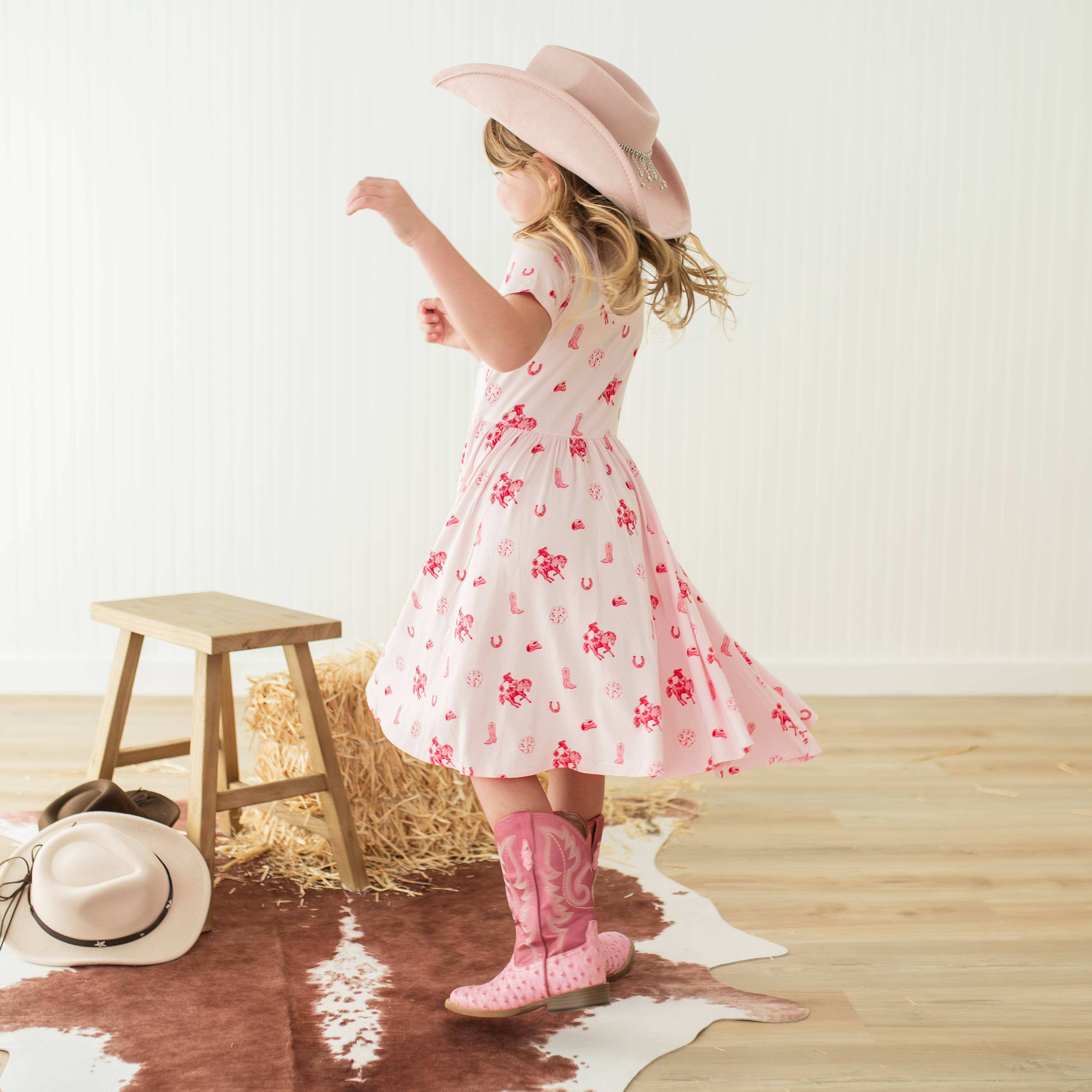 Young girl twirling wearing the Twirl Dress in Disco Cowgirl with a pink cowboy hat