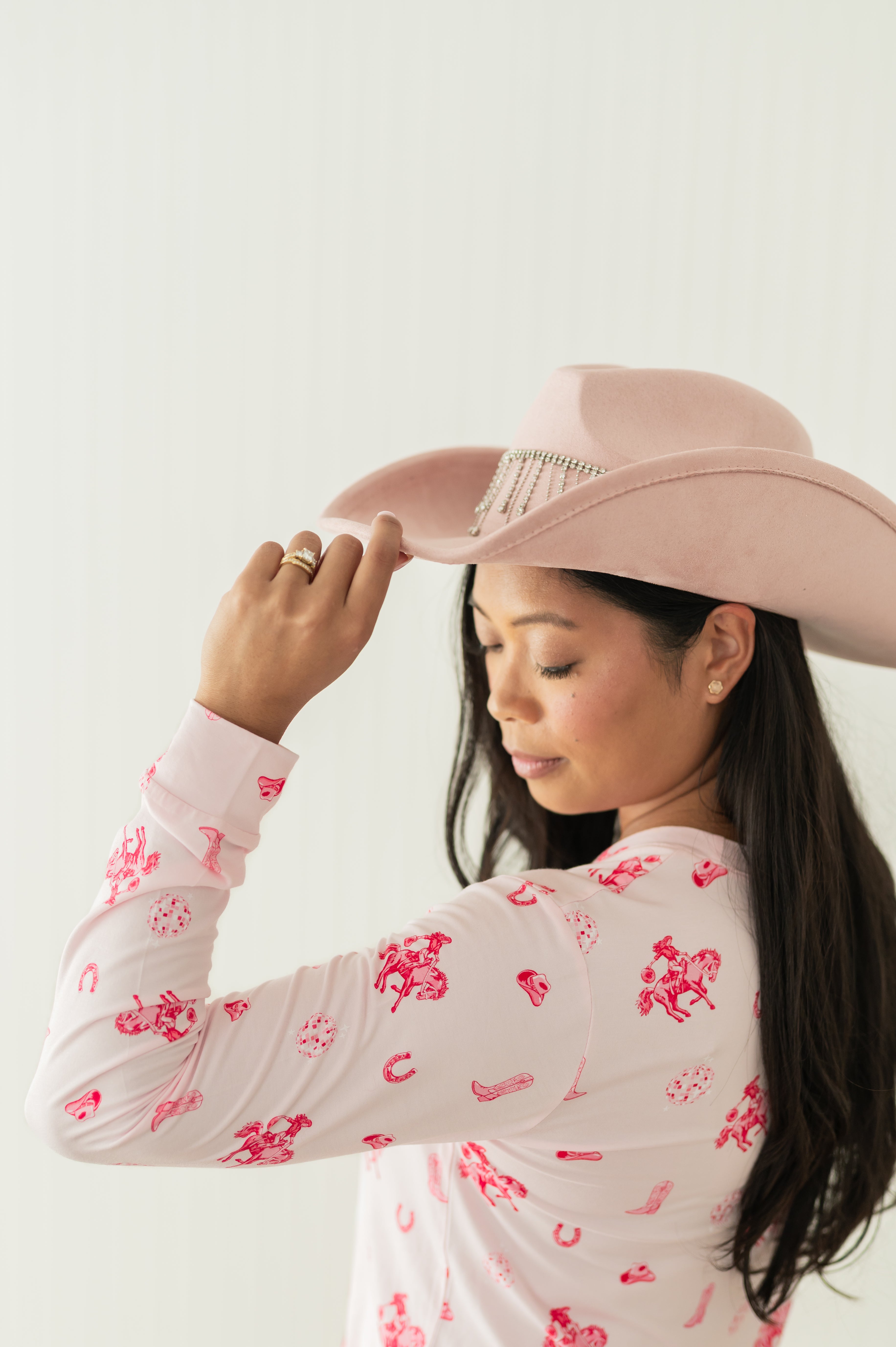 Female model wearing the Women's Jogger Pajama Set in Disco Cowgirl touching the brim of her pink cowboy hat