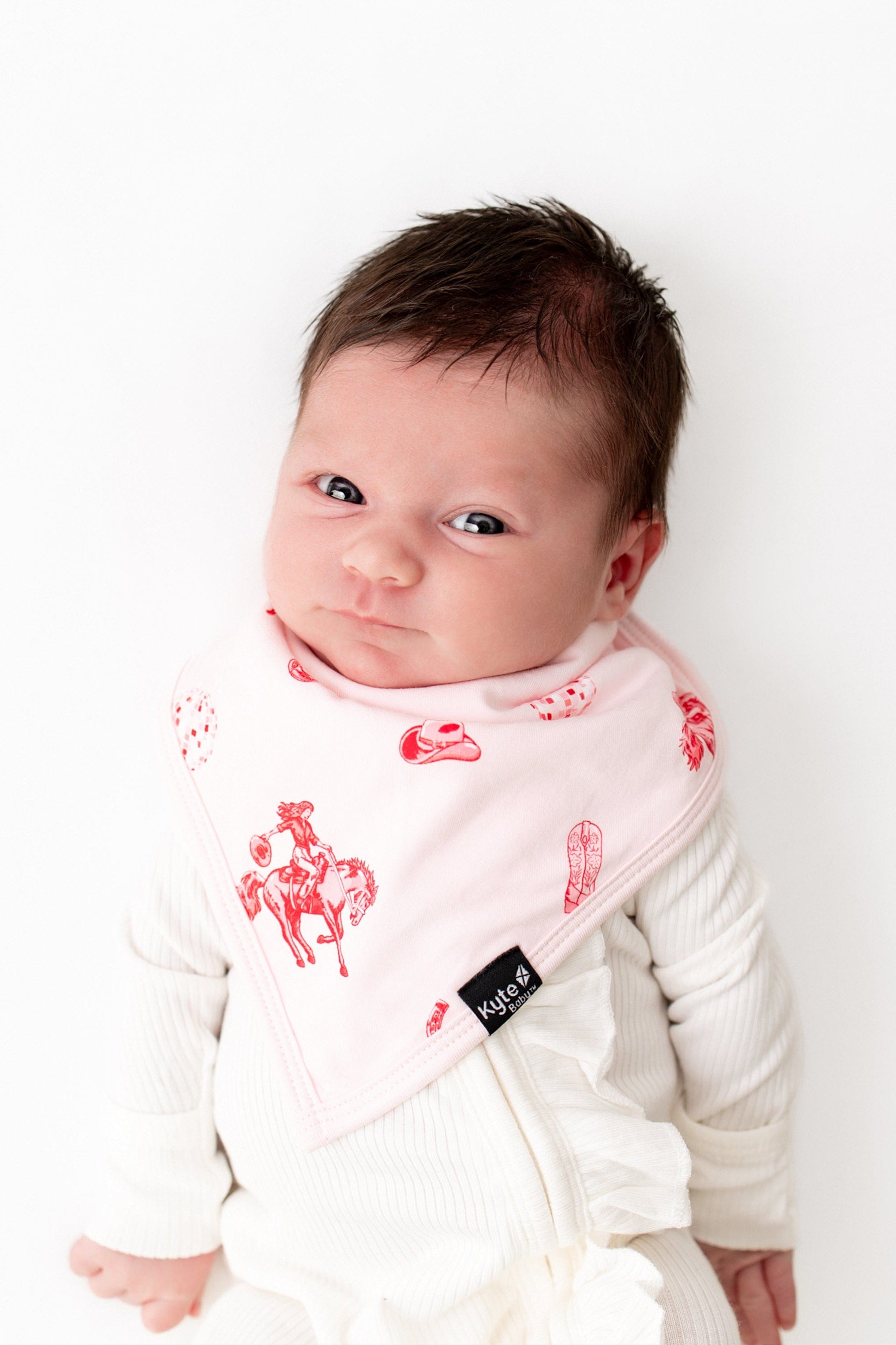 Newborn laying on a white background wearing the absorbant Bib in Disco Cowgirl