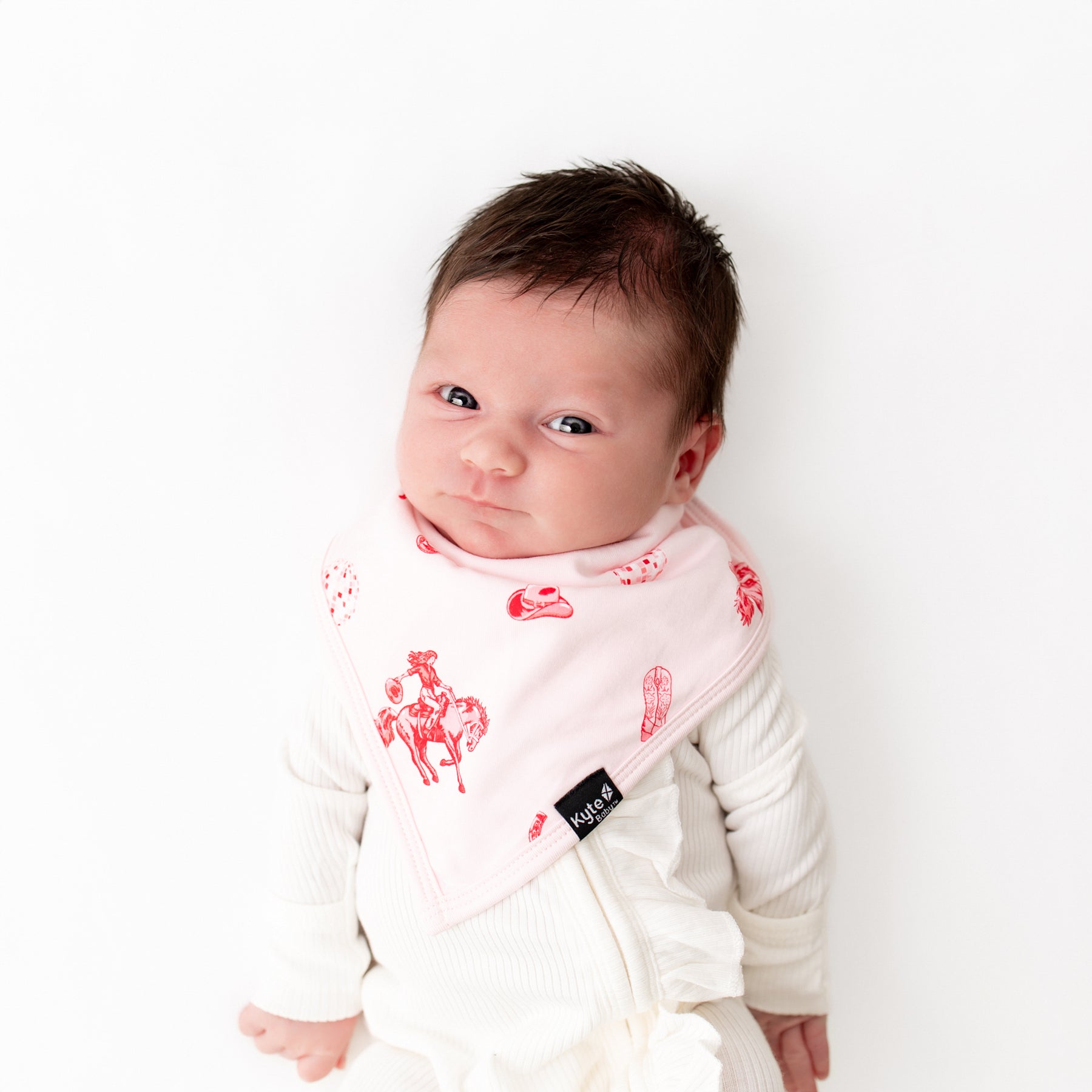 Newborn laying on a white background wearing the absorbant Bib in Disco Cowgirl