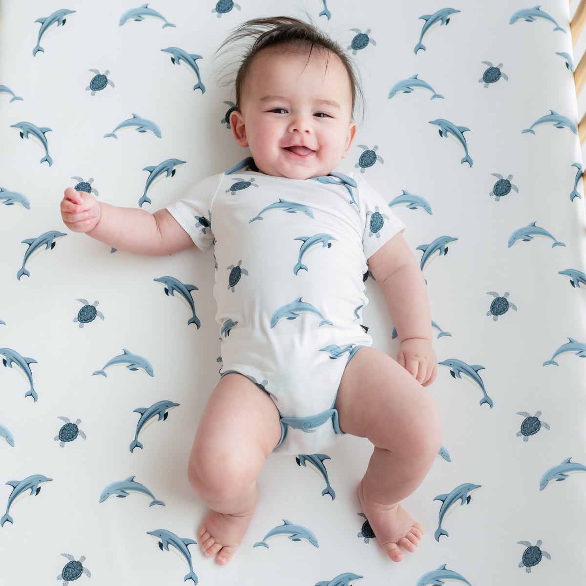 Baby laying on crib with Dolphin crib sheet wearing bodysuit in Dolphin