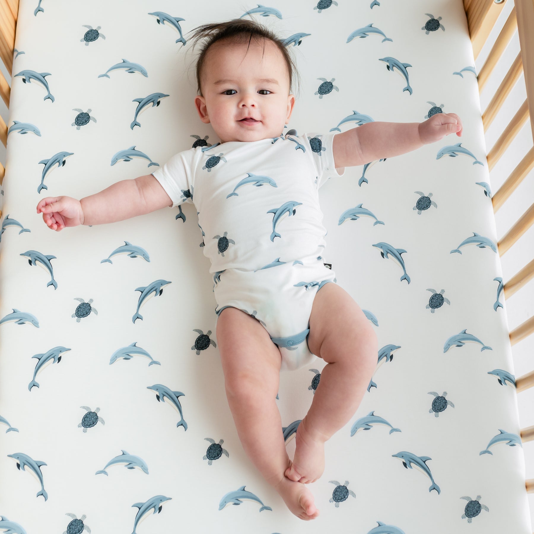 Baby laying on crib with Dolphin crib sheet wearing bodysuit in Dolphin