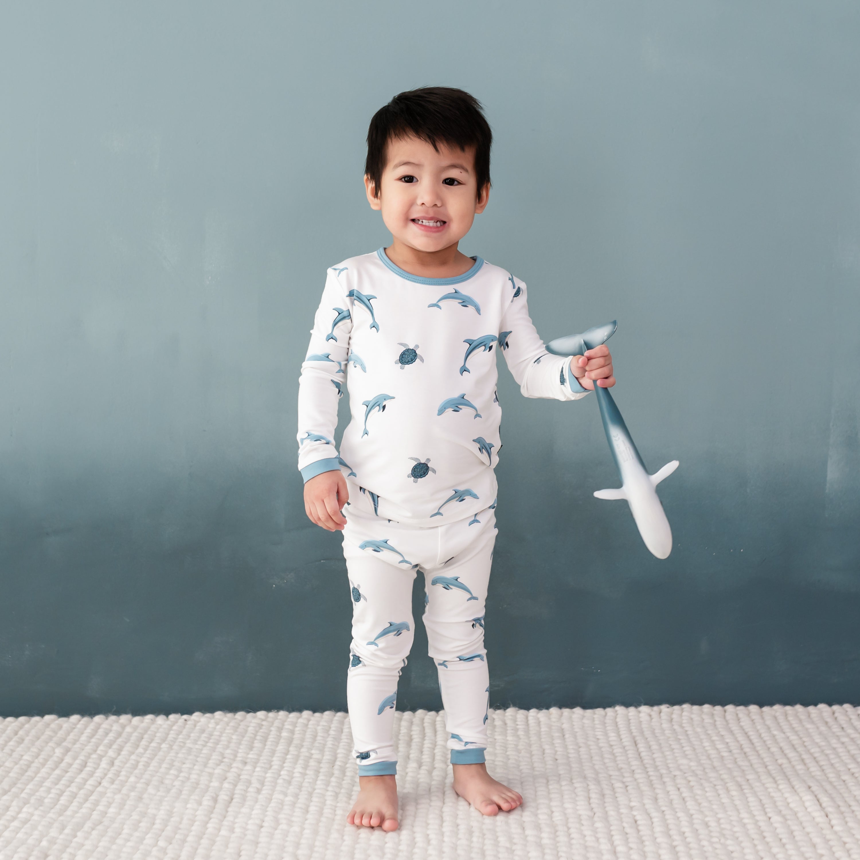 Toddler modeling Long Sleeve Pajamas in Dolphin holding toy whale