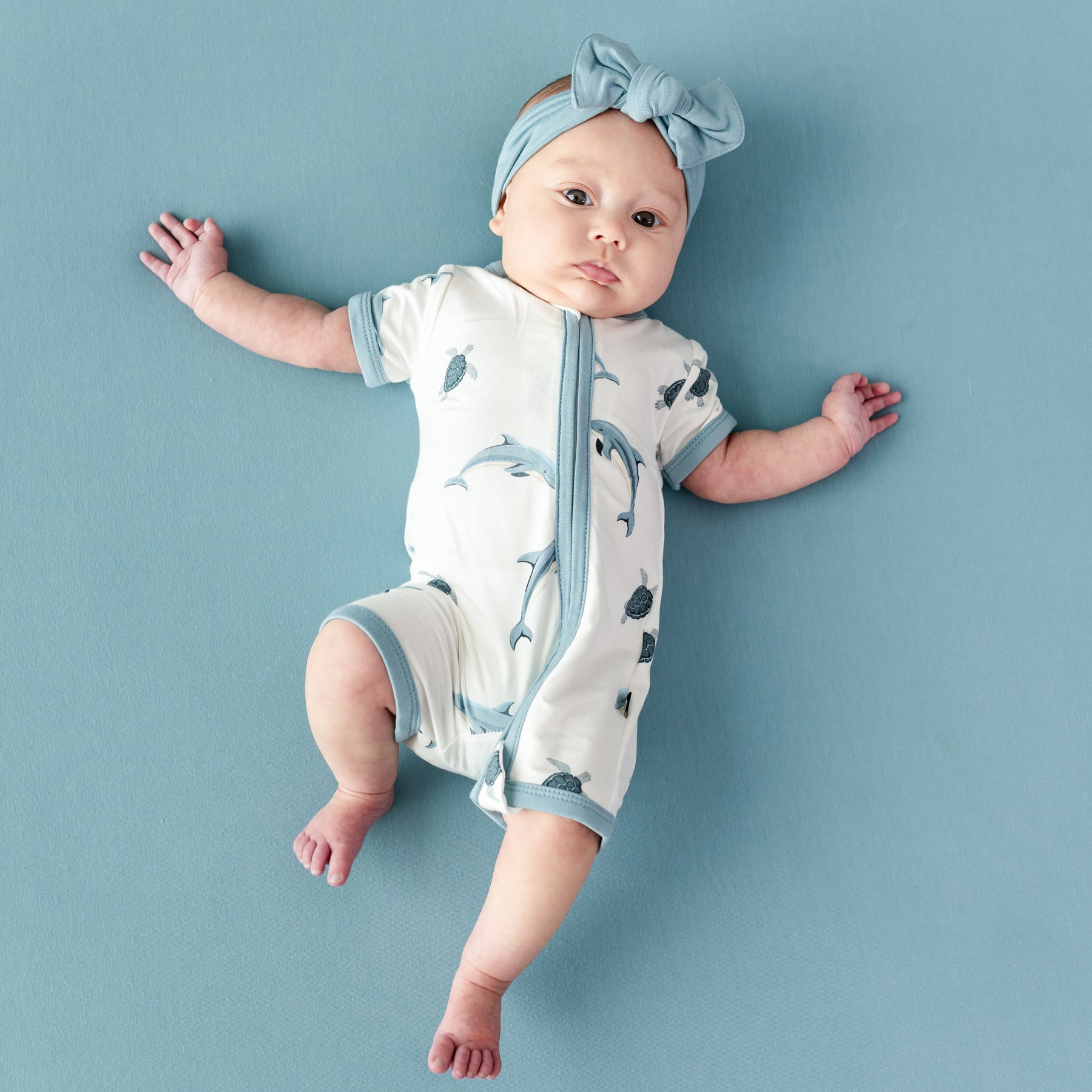 Baby wearing Zipper Shortall Romper in Dolphin and Dusty Blue Bow