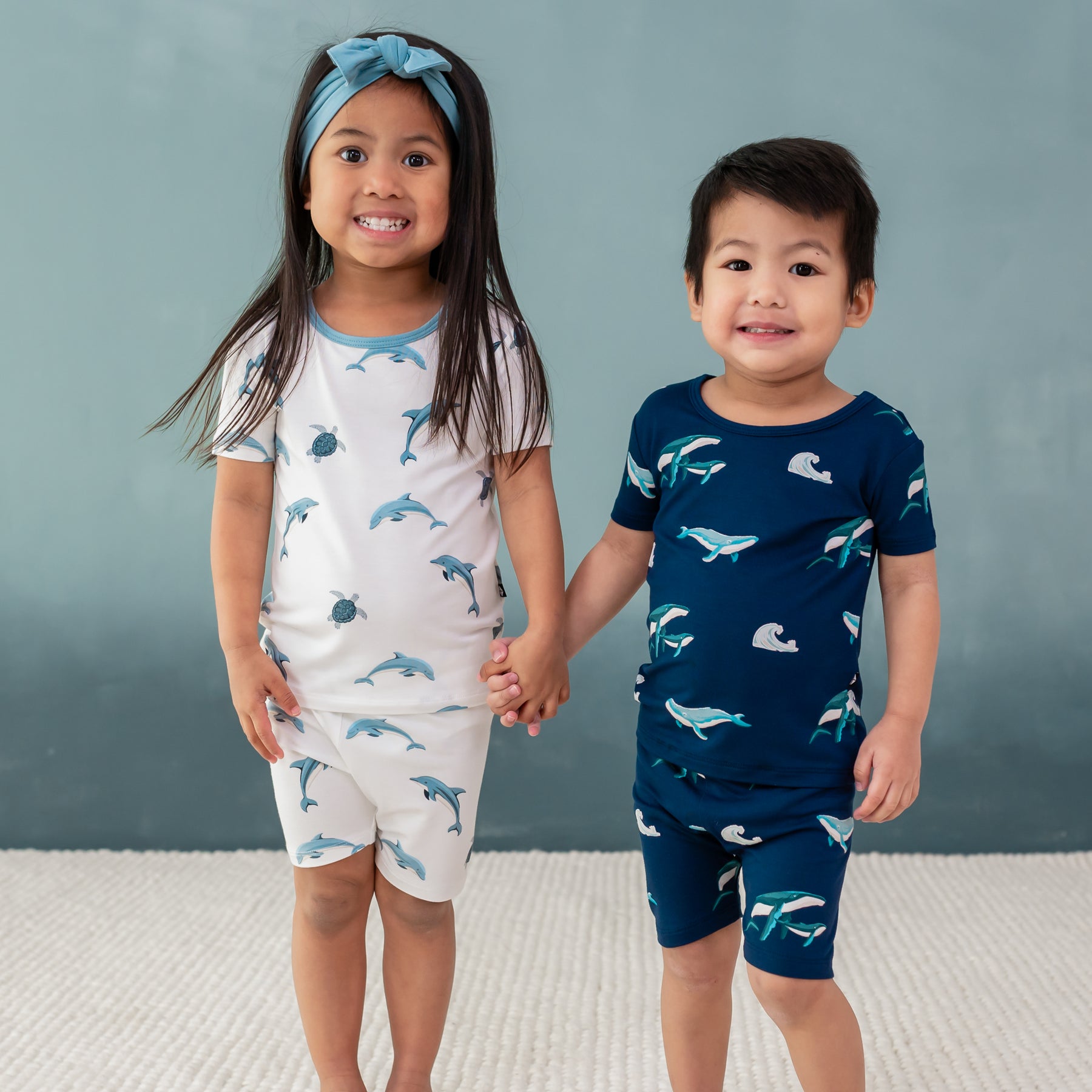 2 toddlers holding hands wearing short sleeve pajamas in dolphin and humpback