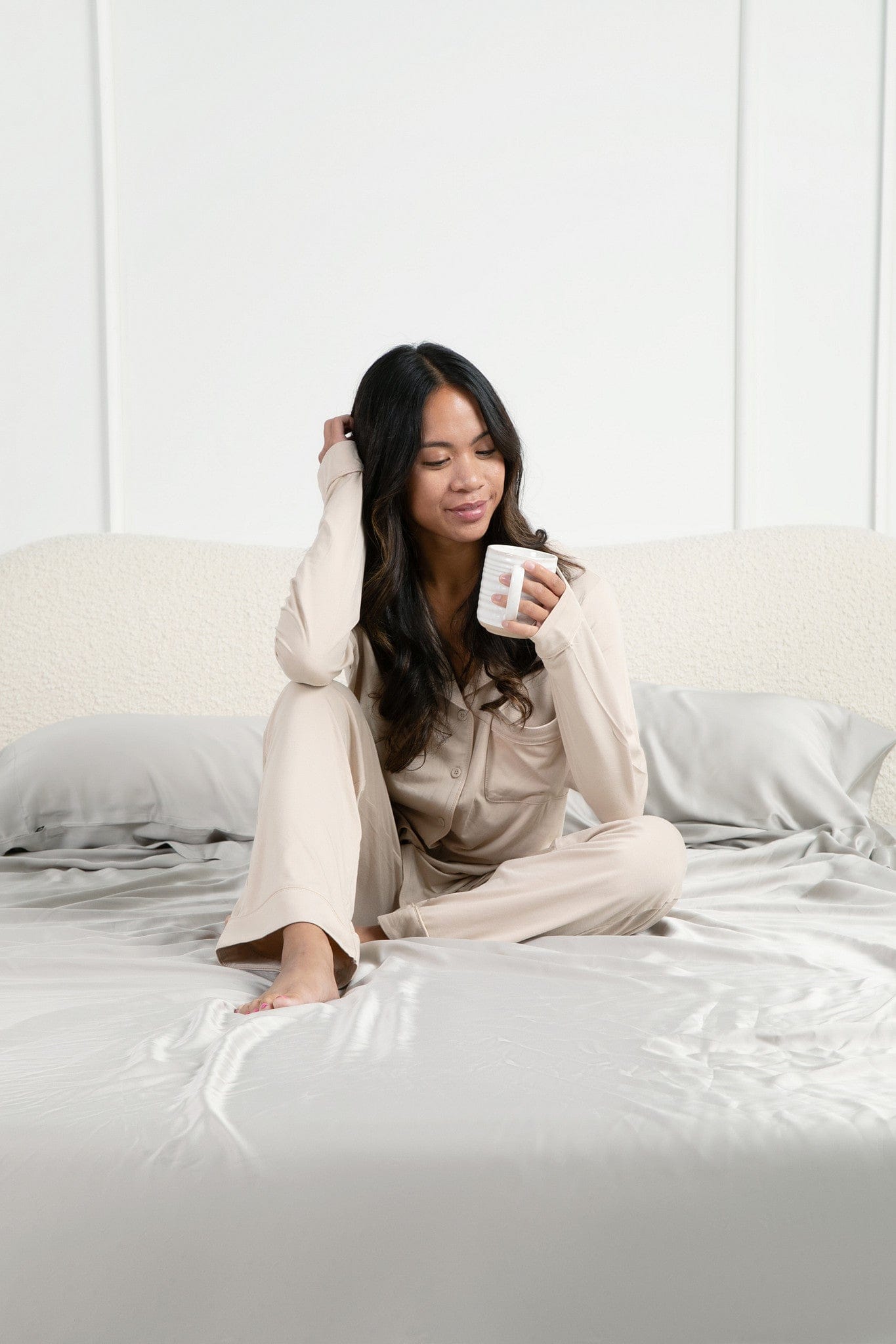 Female model sitting in bed on the Bamboo Sateen Sheet Set in Dove Gray holding a cup of coffee