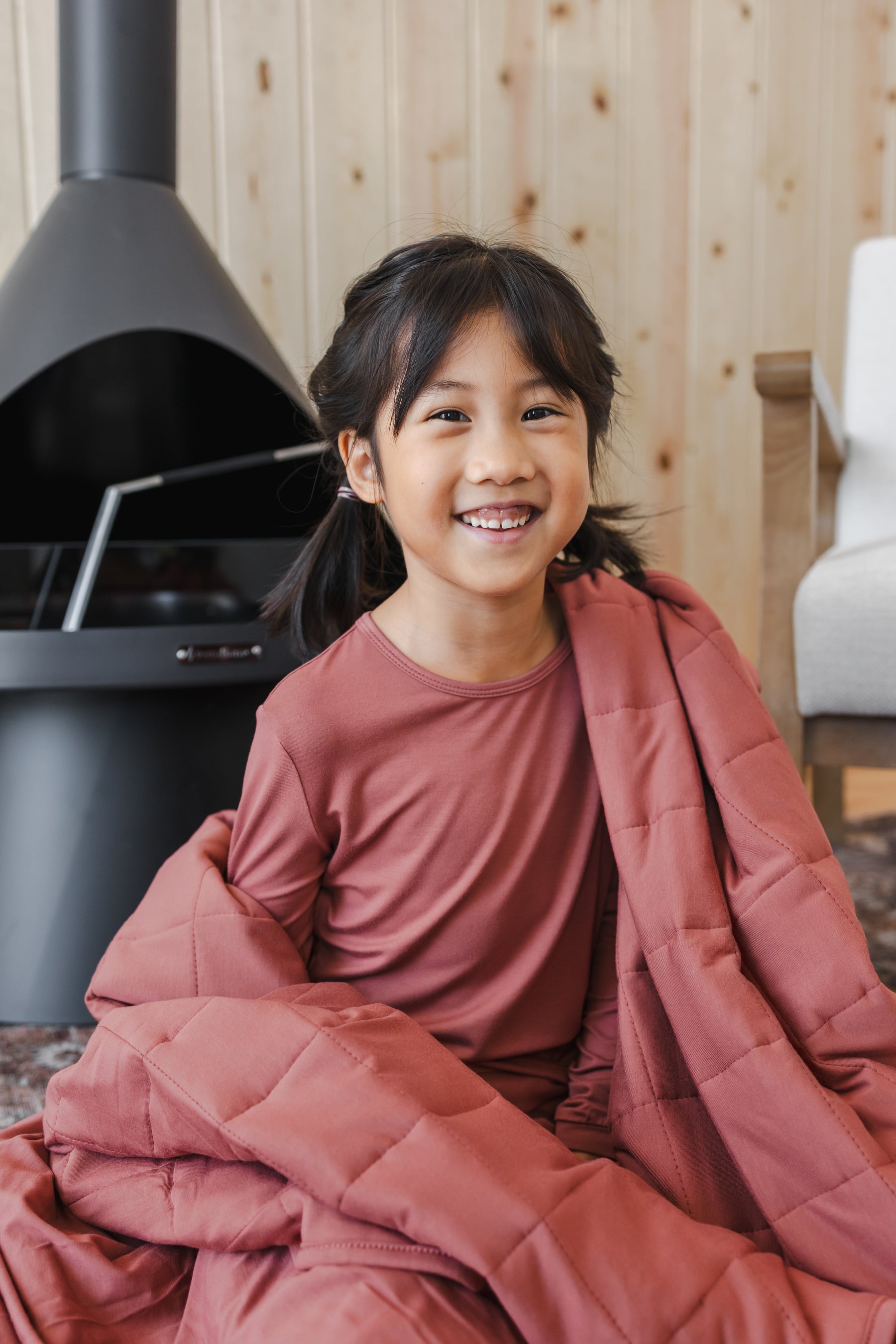 Close up of Girl smiling while wrapped in Youth Blanket in Ember 2.5 wearing a similar color shirt