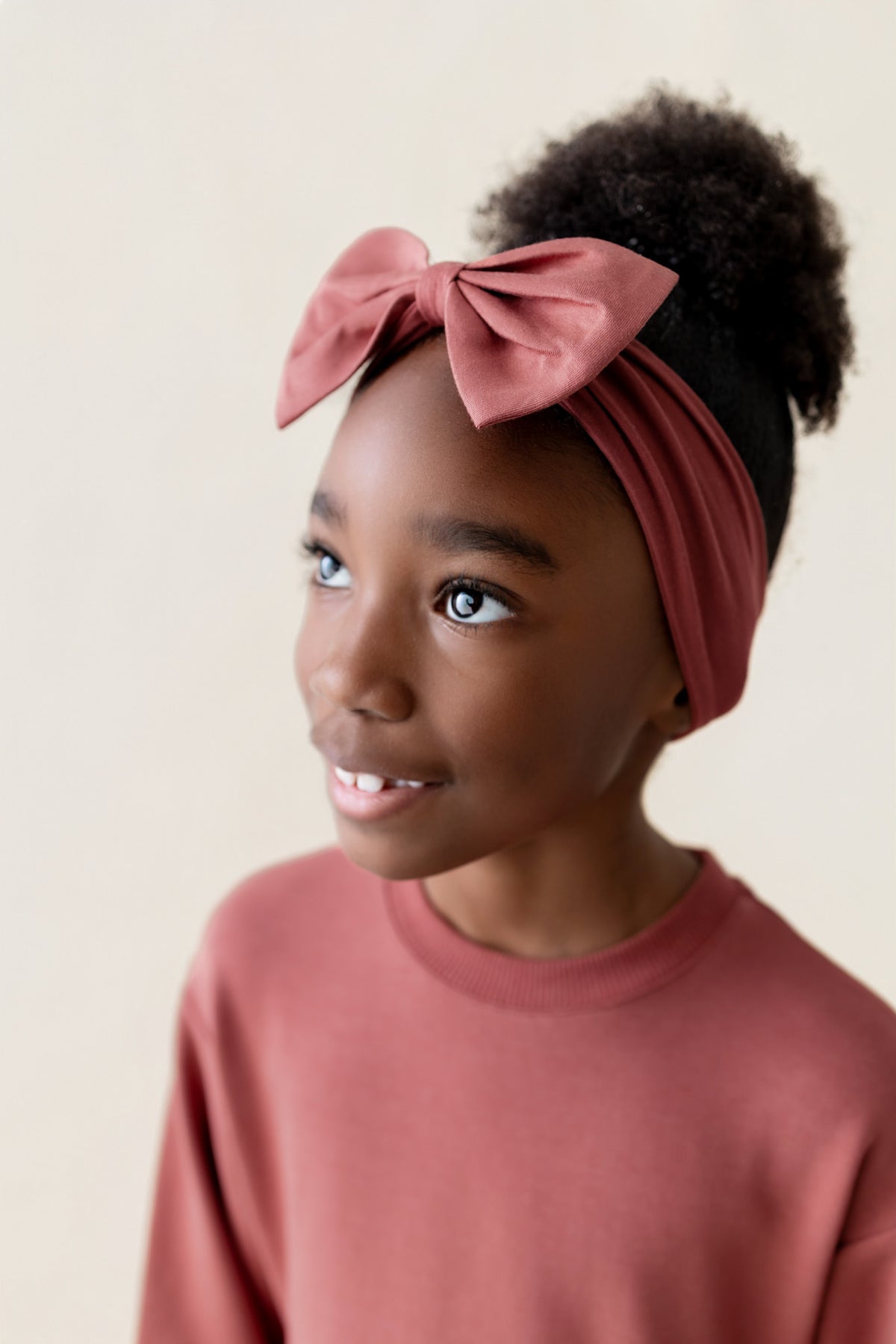 Girl wearing Long Sleeve Skater Dress in Ember color with knotted bow headband on a beige background