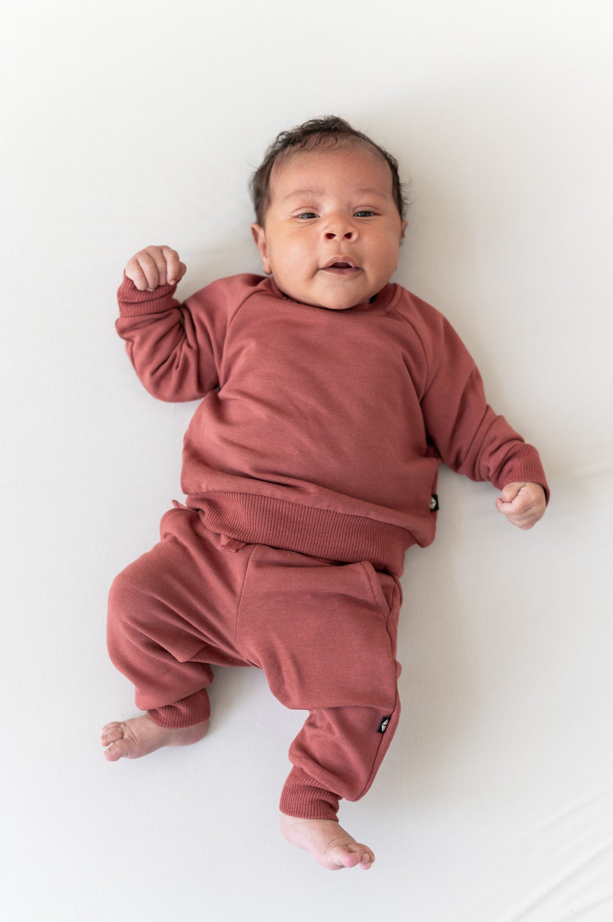Baby wearing Long Sleeve Jogger Set in Ember color on a beige background