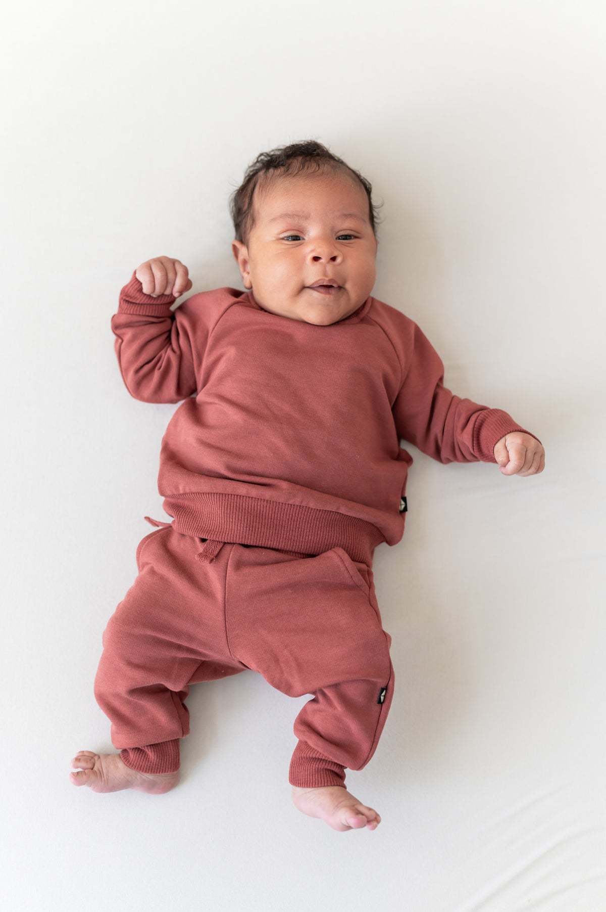 Baby wearing Long Sleeve Jogger Set in Ember color on a beige background