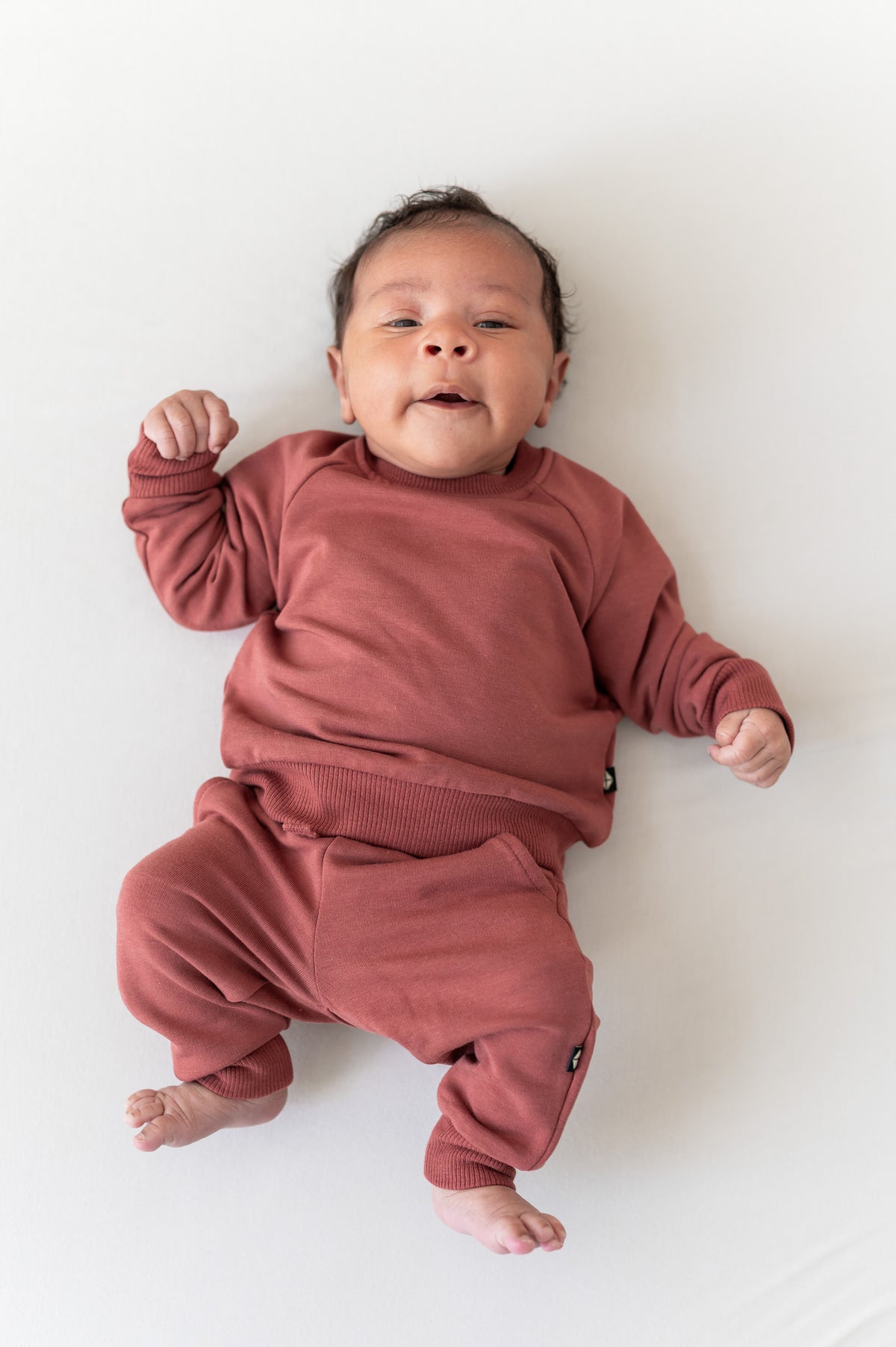 Baby wearing Long Sleeve Jogger Set in Ember color on a beige background