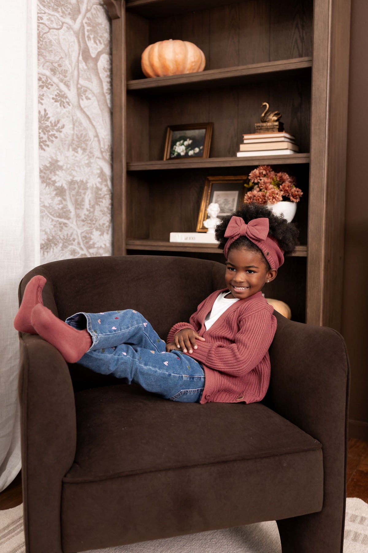 Girl lying on a brown sofa wearing Chunky Knit Oversized Cardigan in Ember over White T-shirt and blue jeans