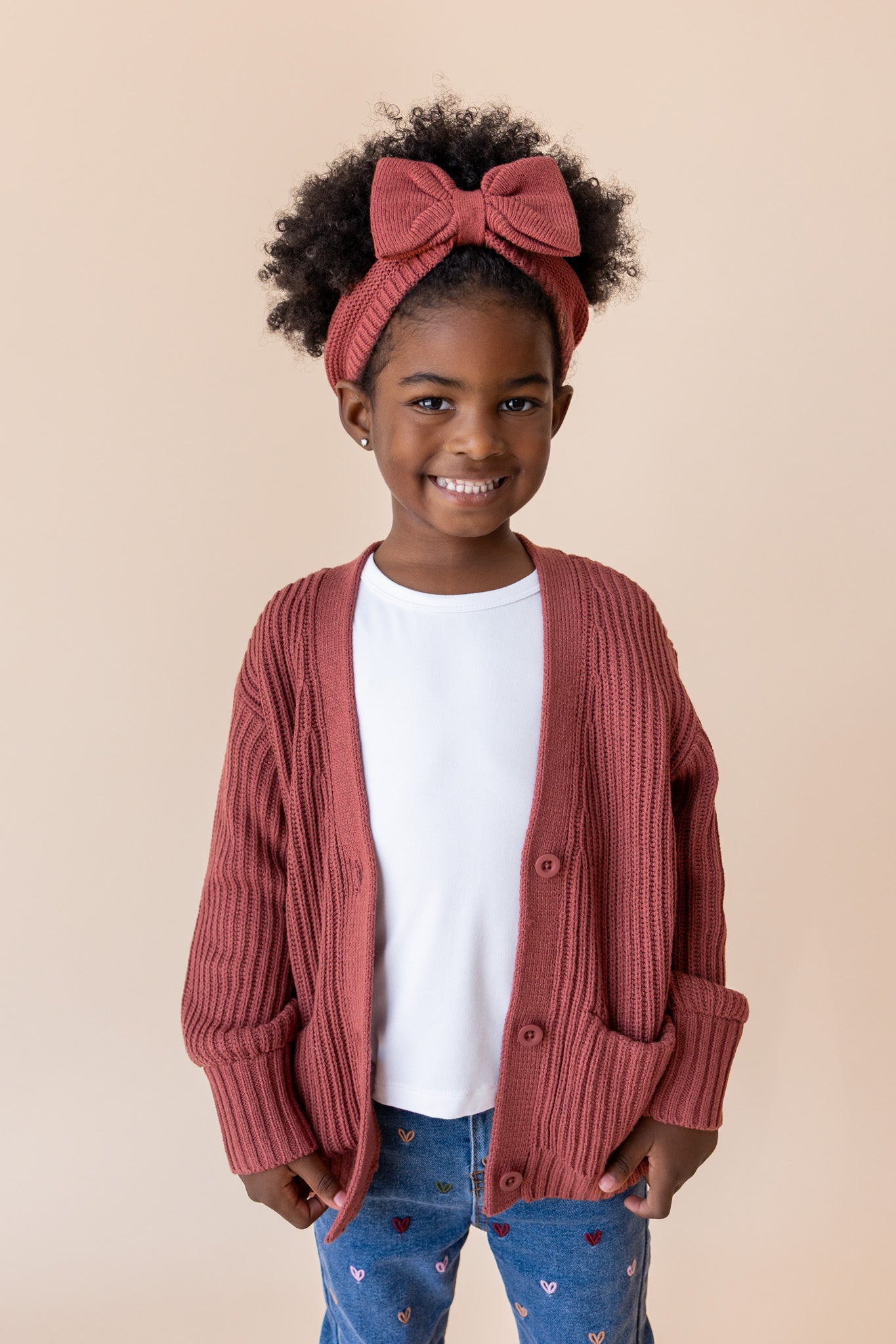 Girl posing in Chunky Knit Oversized Cardigan in Ember over White T-shirt and blue jean on a beige background