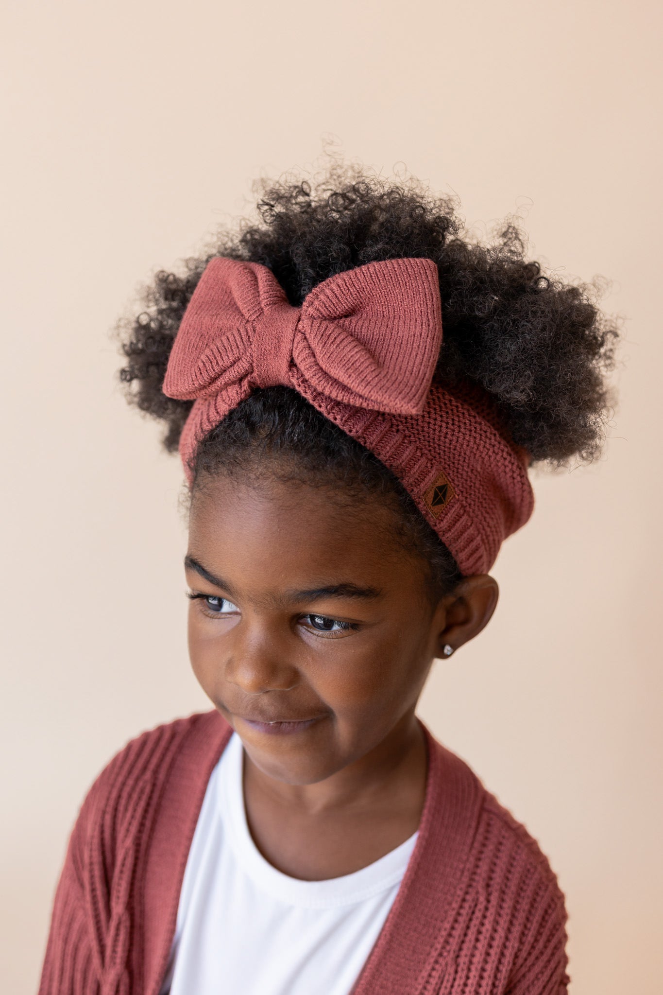 Child wearing Chunky Knit Bow Headband in Ember over White T-shirt and chunky knit oversized cardigan in ember on a beige background