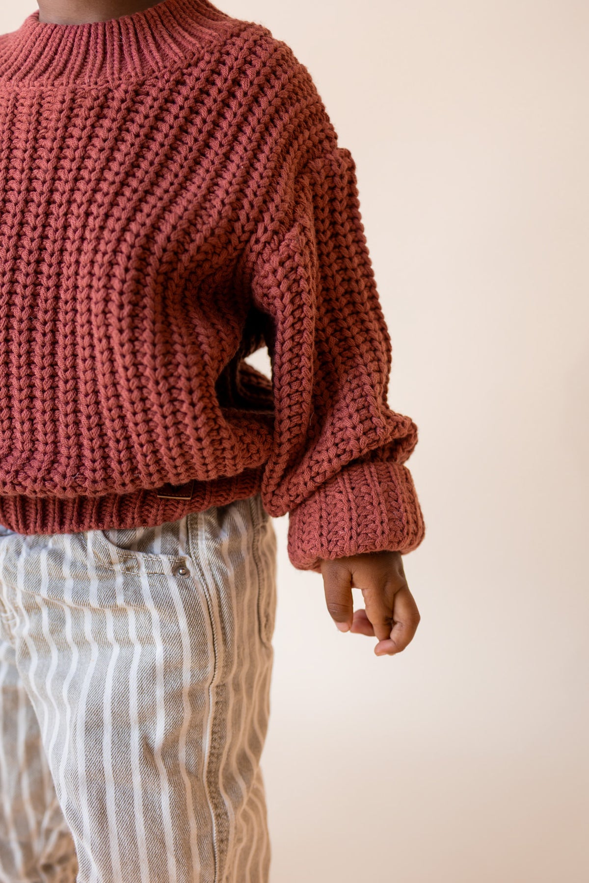 Child wearing Chunky Knit Sweater in Ember over beige pants on a beige background