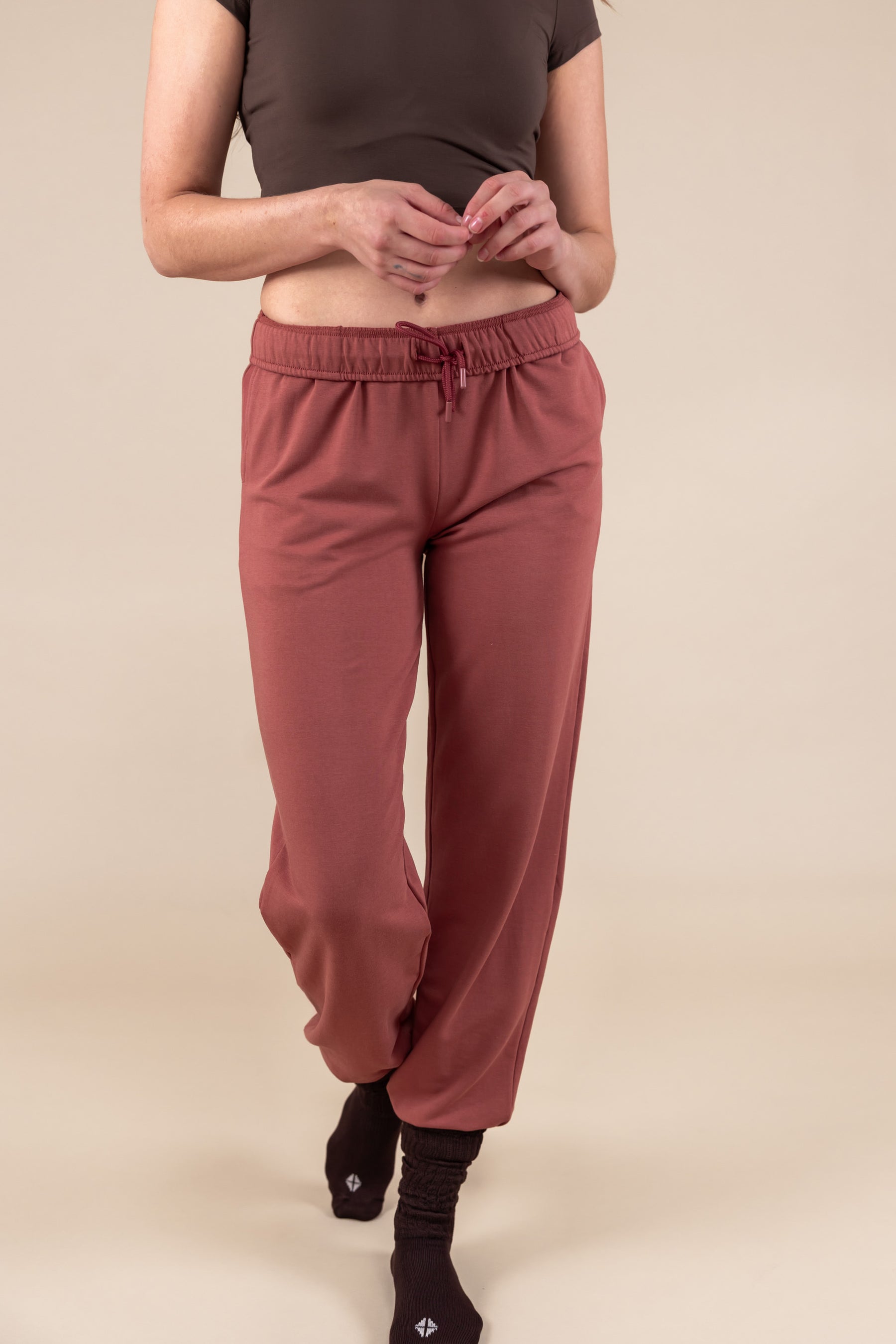 Modal wearing Women's Jogger Pant in Ember color under a brown shirt on a beige background