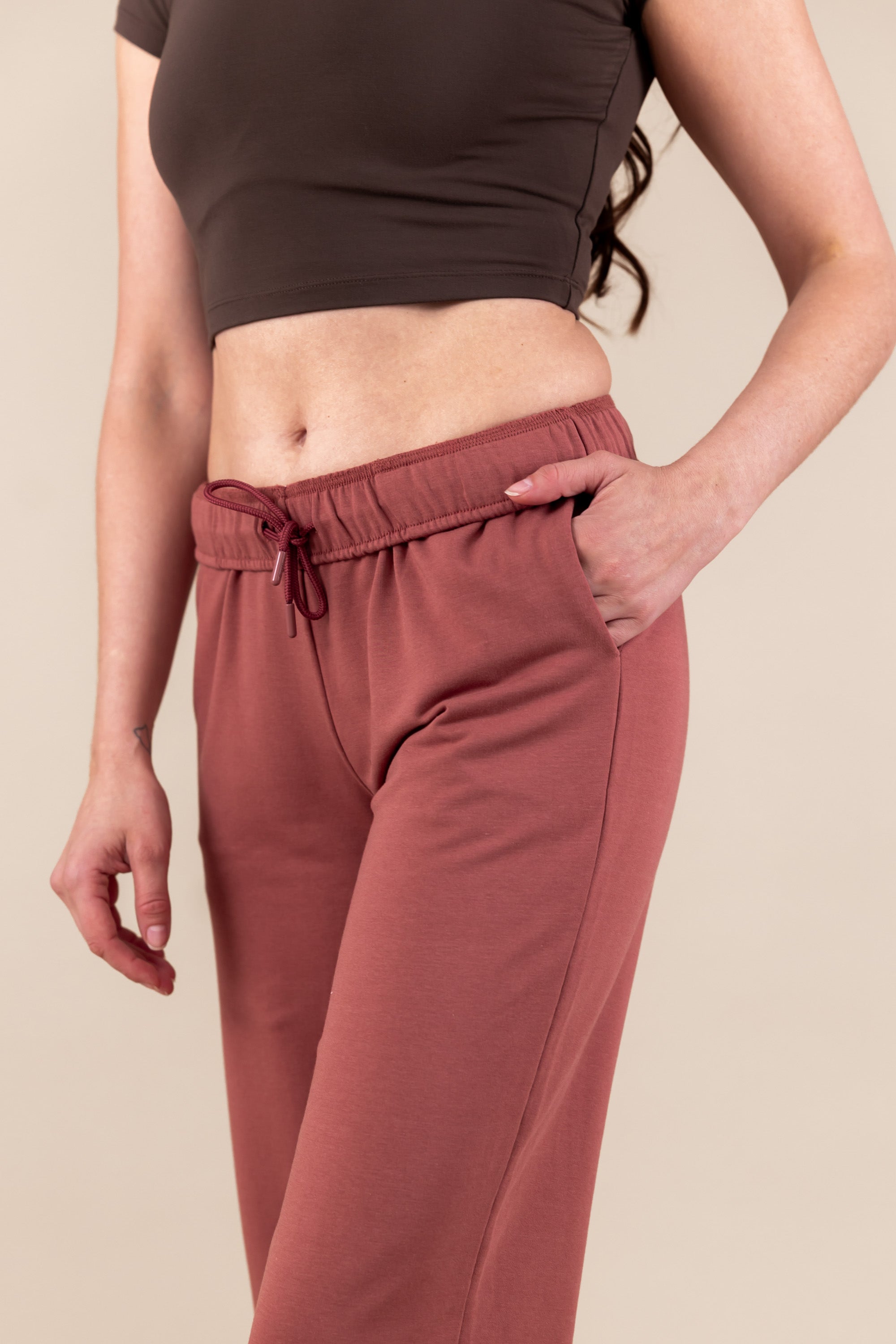 Woman wearing Women's Jogger Pant in Ember color with pockets under a brown shirt on a beige background