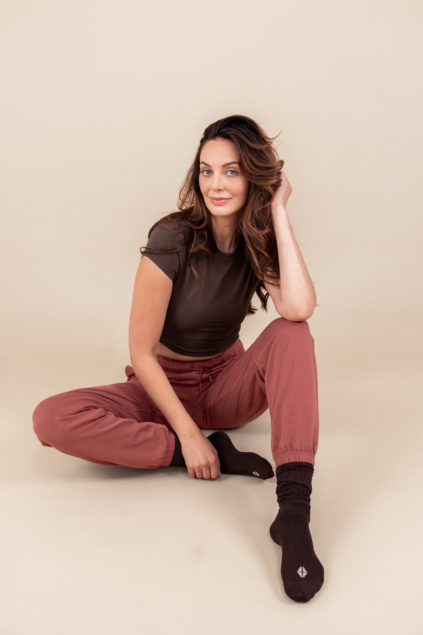 Woman wearing Women's Jogger Pant in Ember color under a brown shirt while sitting on a beige floor and background
