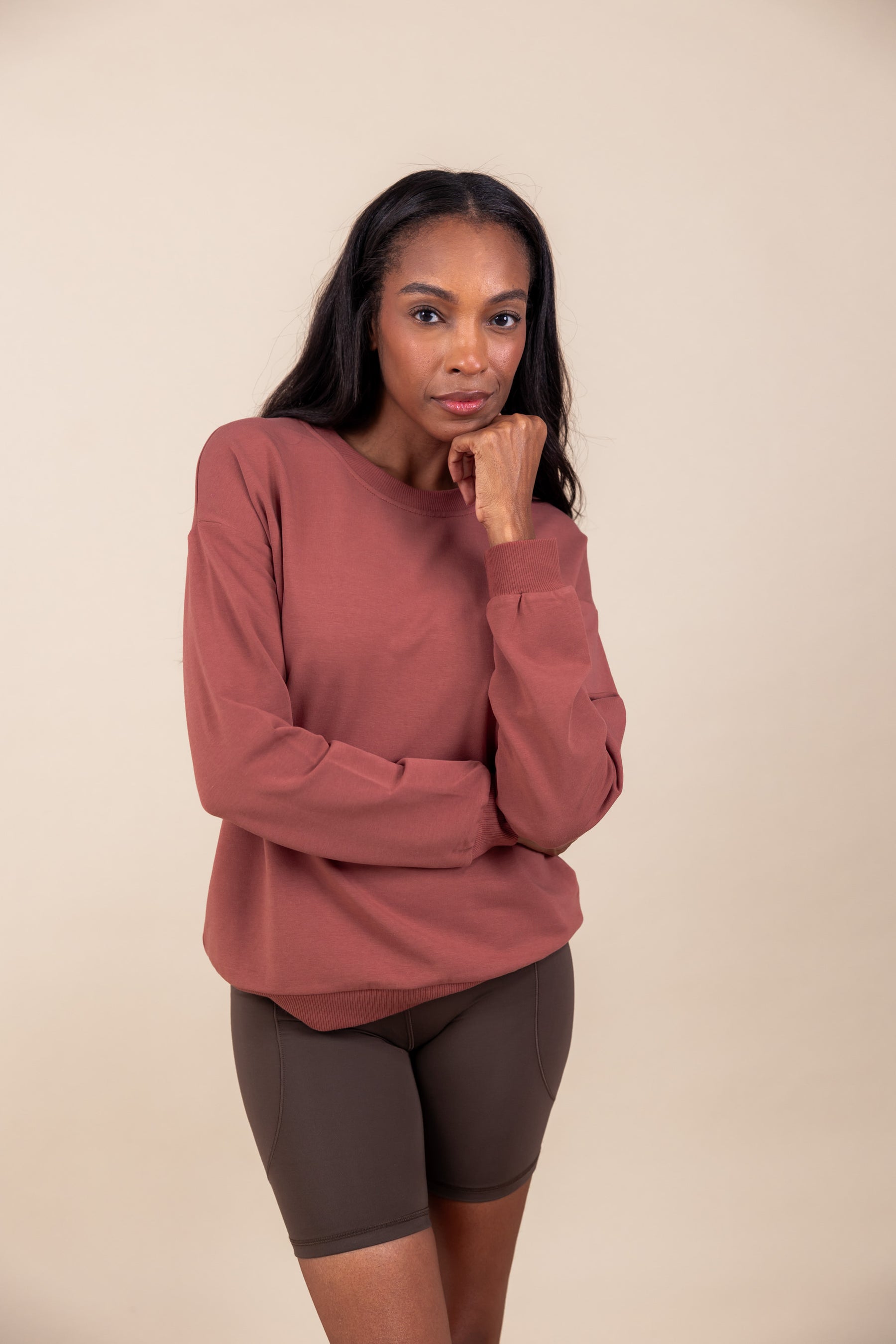 Woman wearing Women's Sweatshirt in Ember color over brown shorts on a beige background