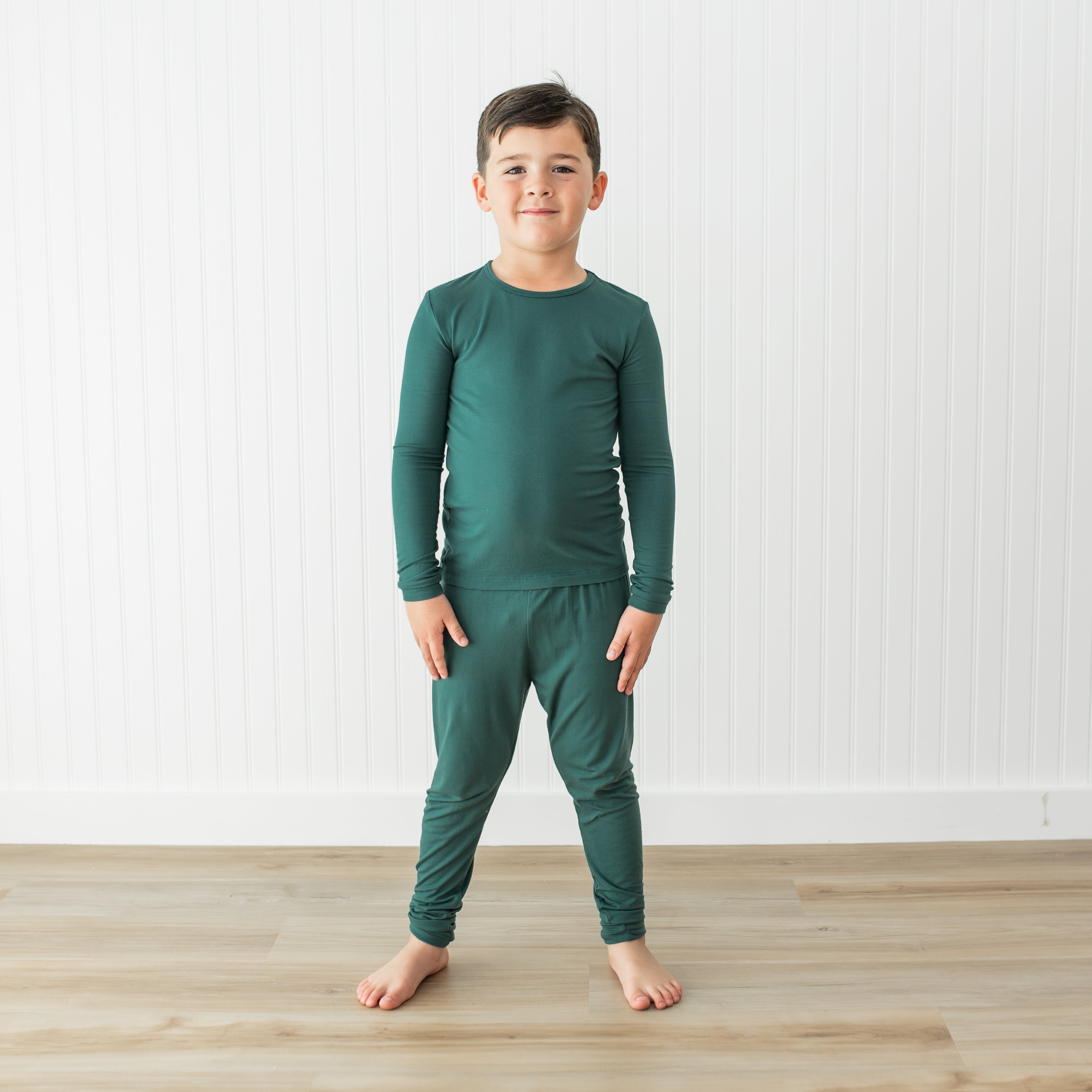 Child wearing a green pajama set standing on a wooden floor with a white background