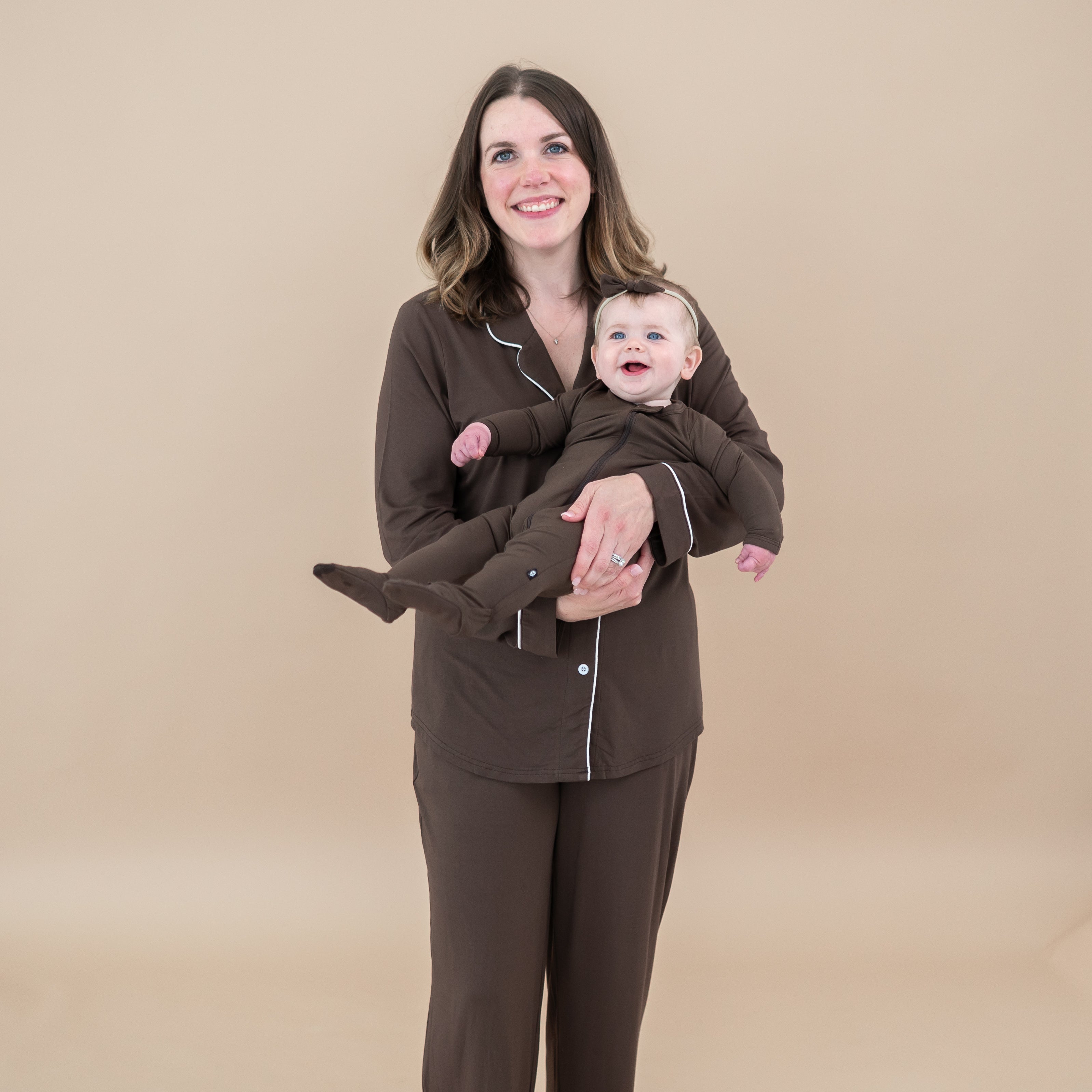 Female model wearing the Long-Sleeved Women's Pajama Set in Espresso with Cloud Trim holding infant girl in matching zippered footie