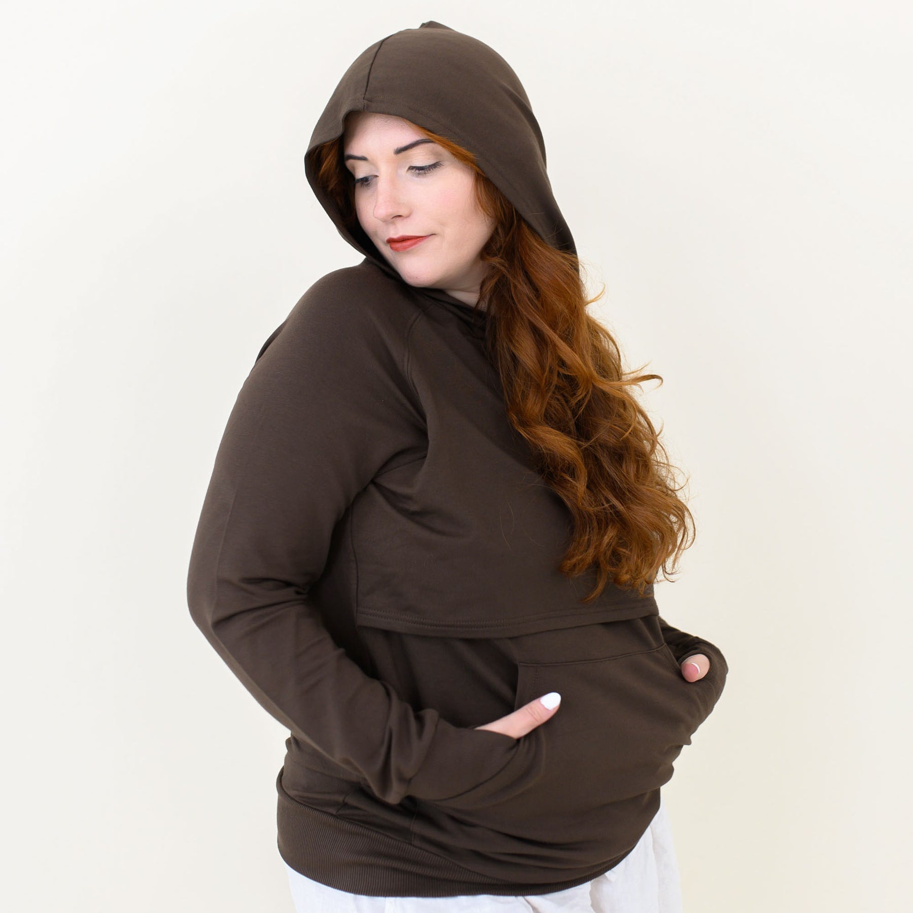 Smiling female wearing the Women's French Terry Nursing Hoodie in Espresso with the hood up and her hands in the kangaroo pocket