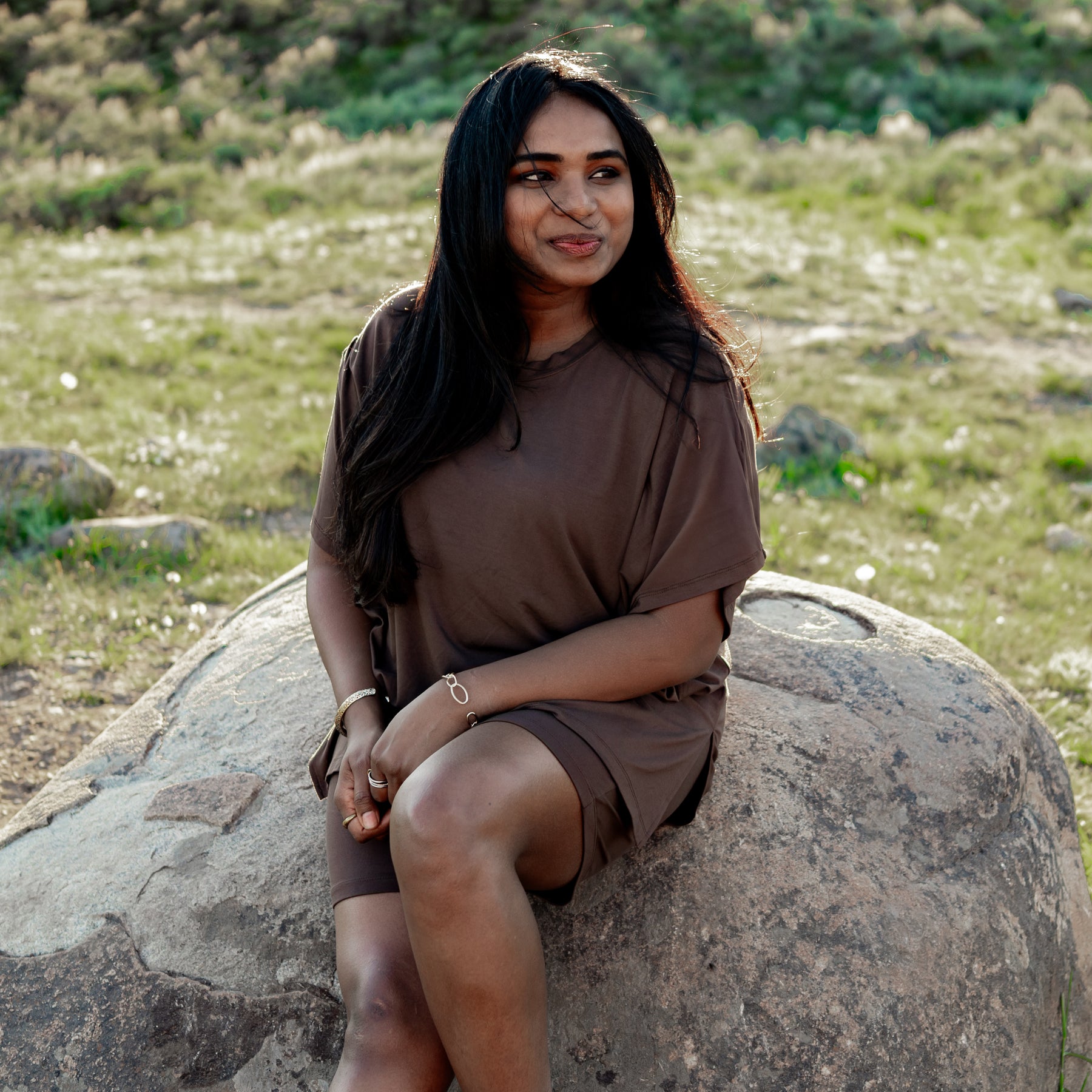 Female model sitting on a boulder wearing the Women’s Biker Short Set in Espresso