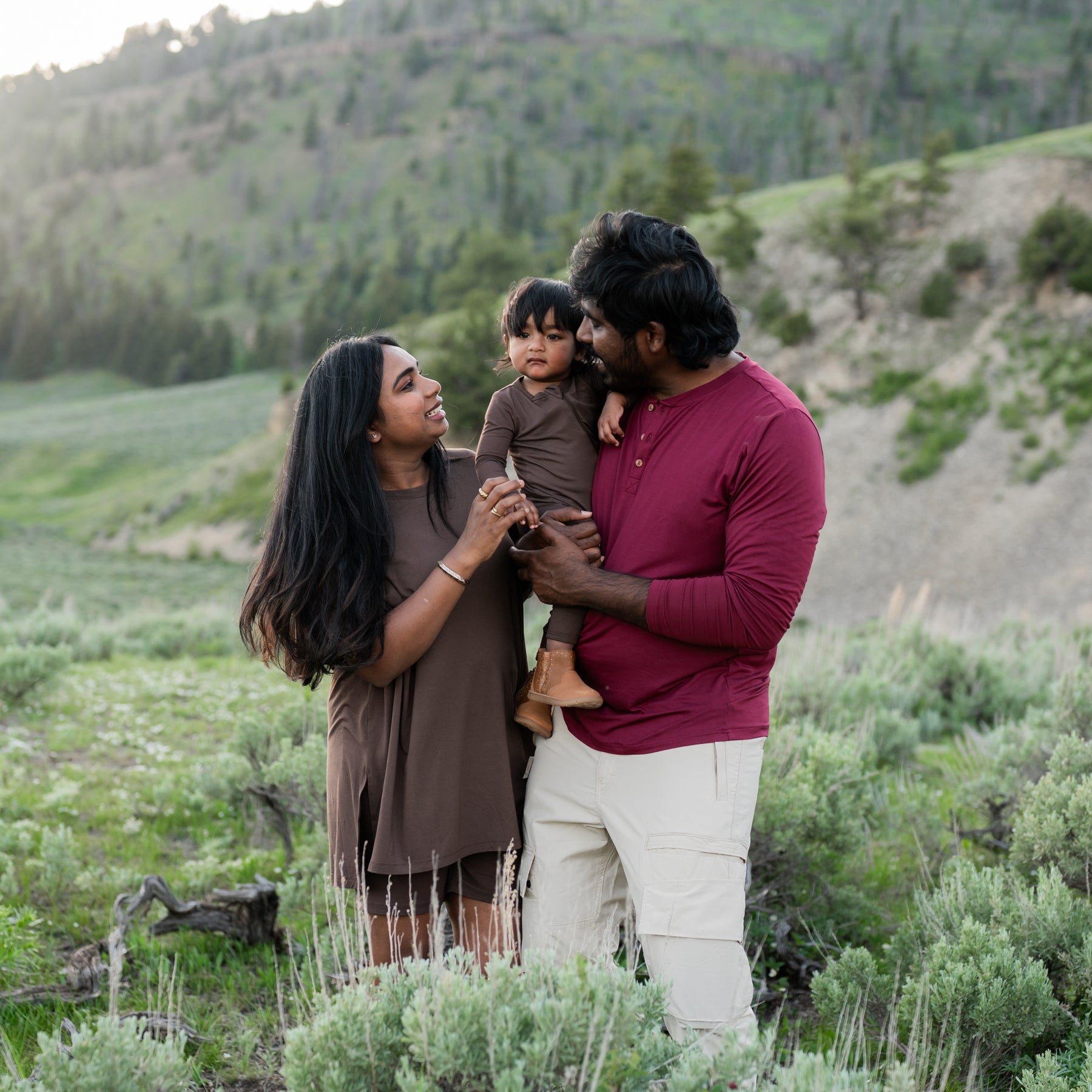 Family wearing colors from the fall collection. Pictured are the Zippered Romper in Espresso, women's biker short set in espresso and men's long sleeve henley tee in burgundy