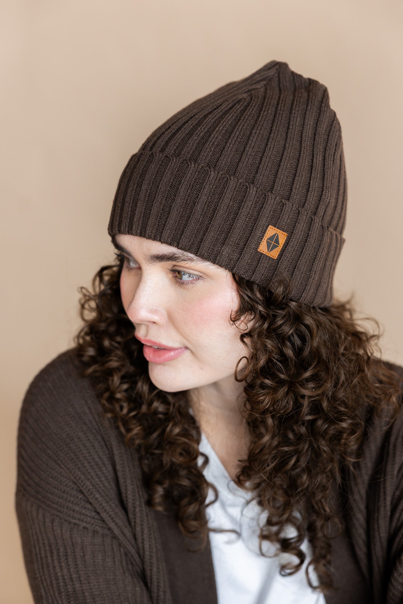 Modal wearing Chunky Knit Adult Ribbed Beanie in Espresso over white T-shirt and chunky knit cardigan in espresso on a beige background