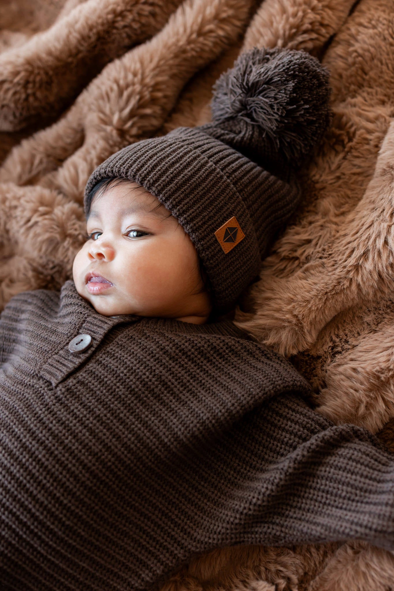 Baby lying on a brown blanket wearing Chunky Knit Pom Beanie and chunky knit romper in Espresso