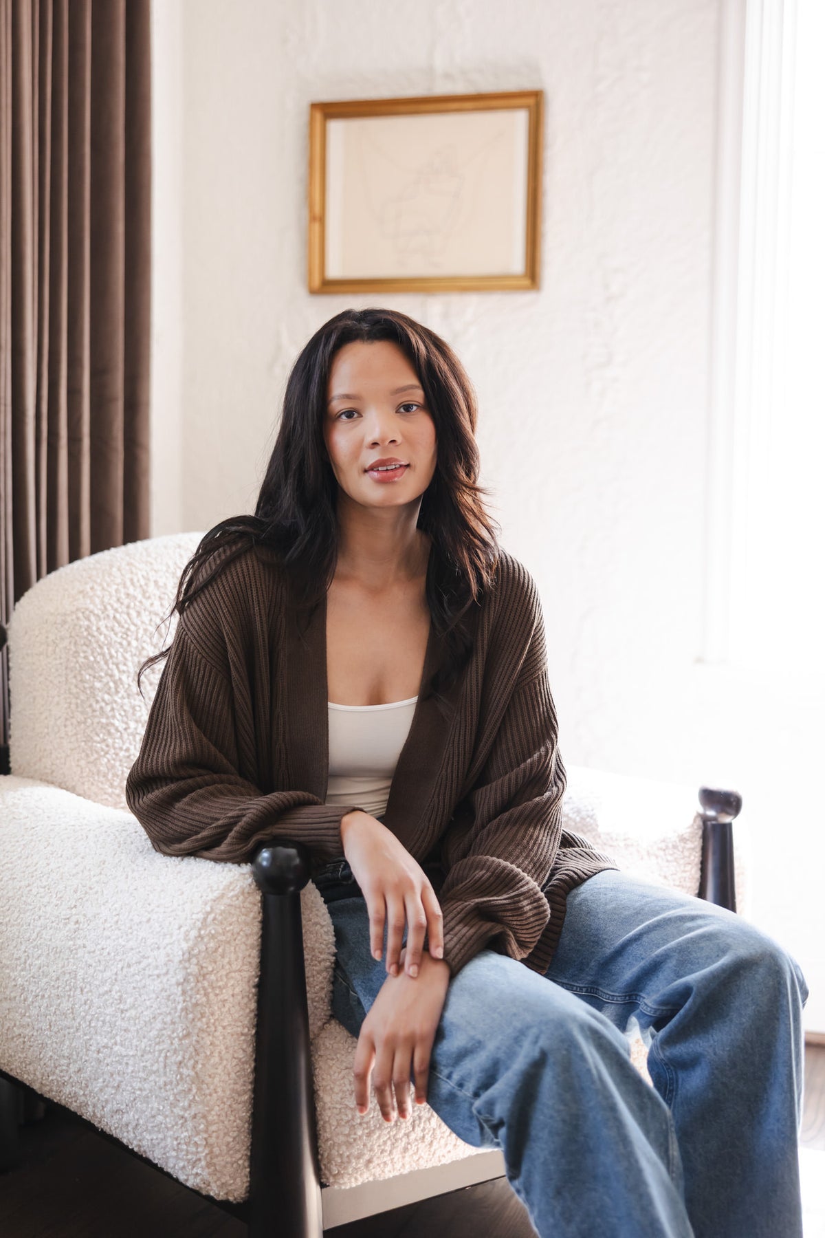 Modal wearing Chunky knit oversized cardigan in espresso over blue jeans and white camisole sitting on a white sofa
