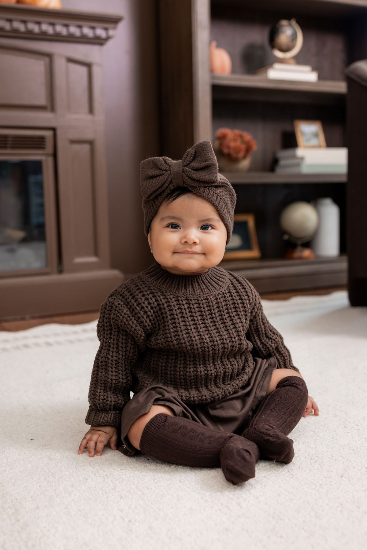 Baby sitting on white carpet wearing Knee High Socks in Espresso under Chunky knit Sweater in Espresso and Chunky Knit Bow headband in Espresso